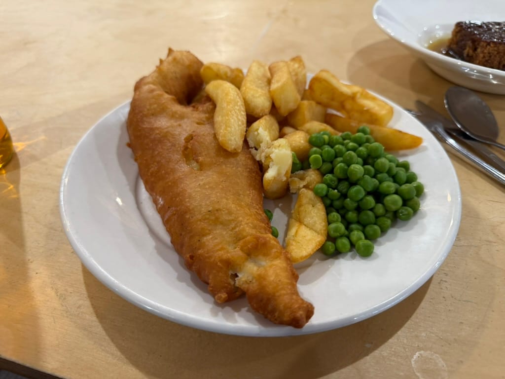 Fish and chips with peas on a white plate.