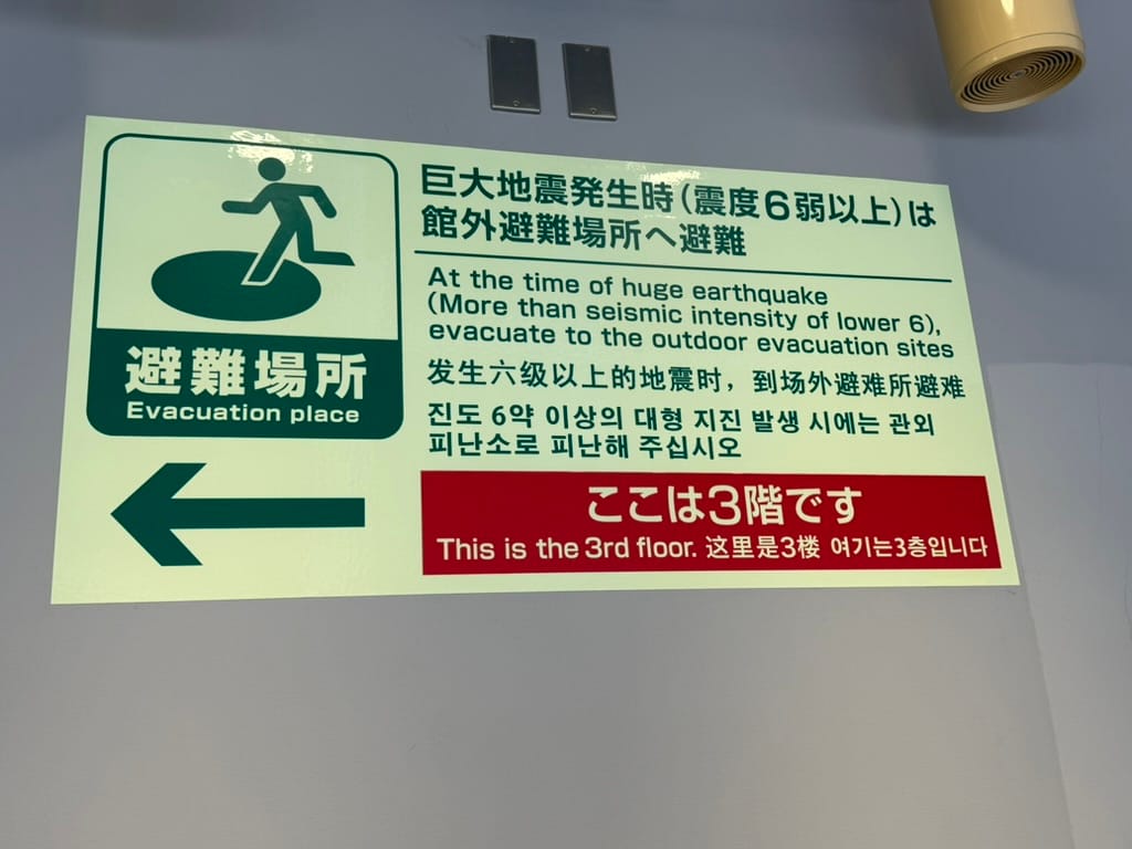 Multilingual emergency evacuation sign at Kansai International Airport, directing people to an outdoor evacuation area during a major earthquake and indicating the third floor.