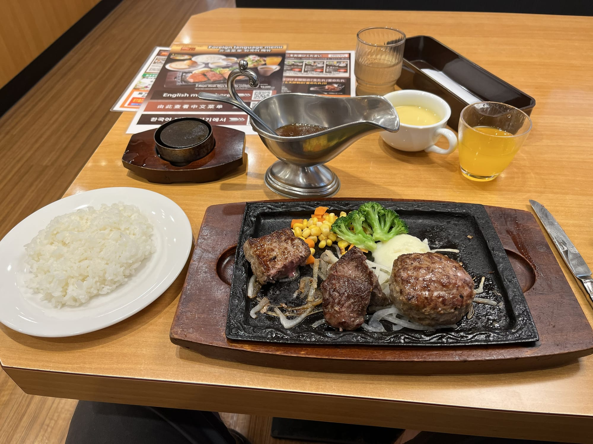 Japanese steak meal served on a sizzling hot plate with rice, vegetables and sauce, accompanied by soup, juice and condiments in a family restaurant.