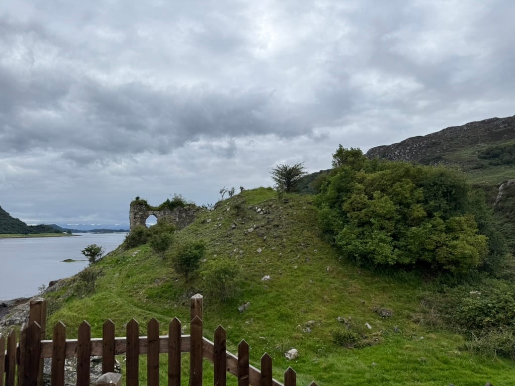 Ruined castle walls on a grassy hillside above a loch.