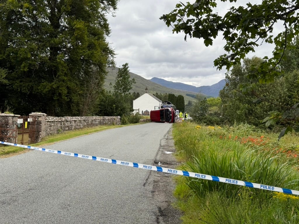Overturned vehicle on a rural road blocked by police tape.