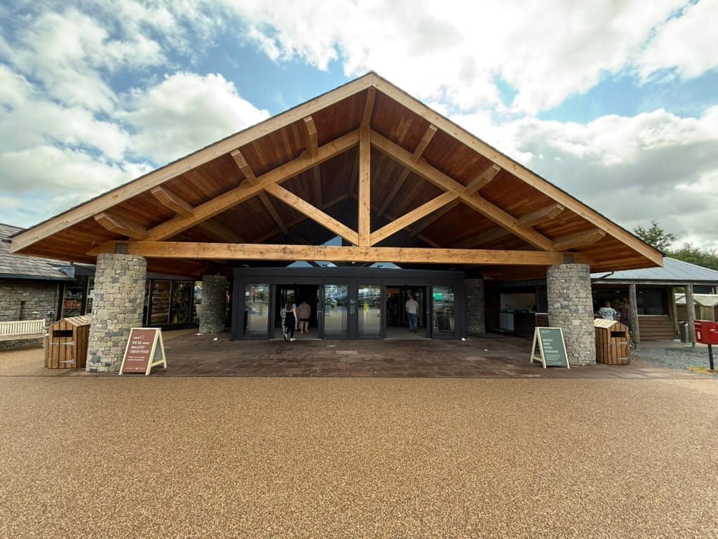 Modern visitor centre entrance with timber roof and stone pillars.