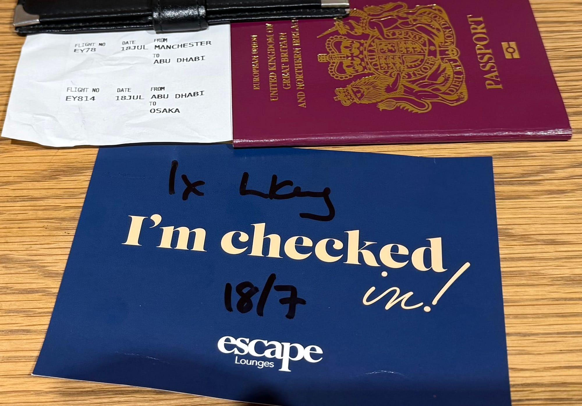 British passport, flight details and an Escape Lounge check-in card on a table at Manchester Airport before departure via Abu Dhabi to Osaka.