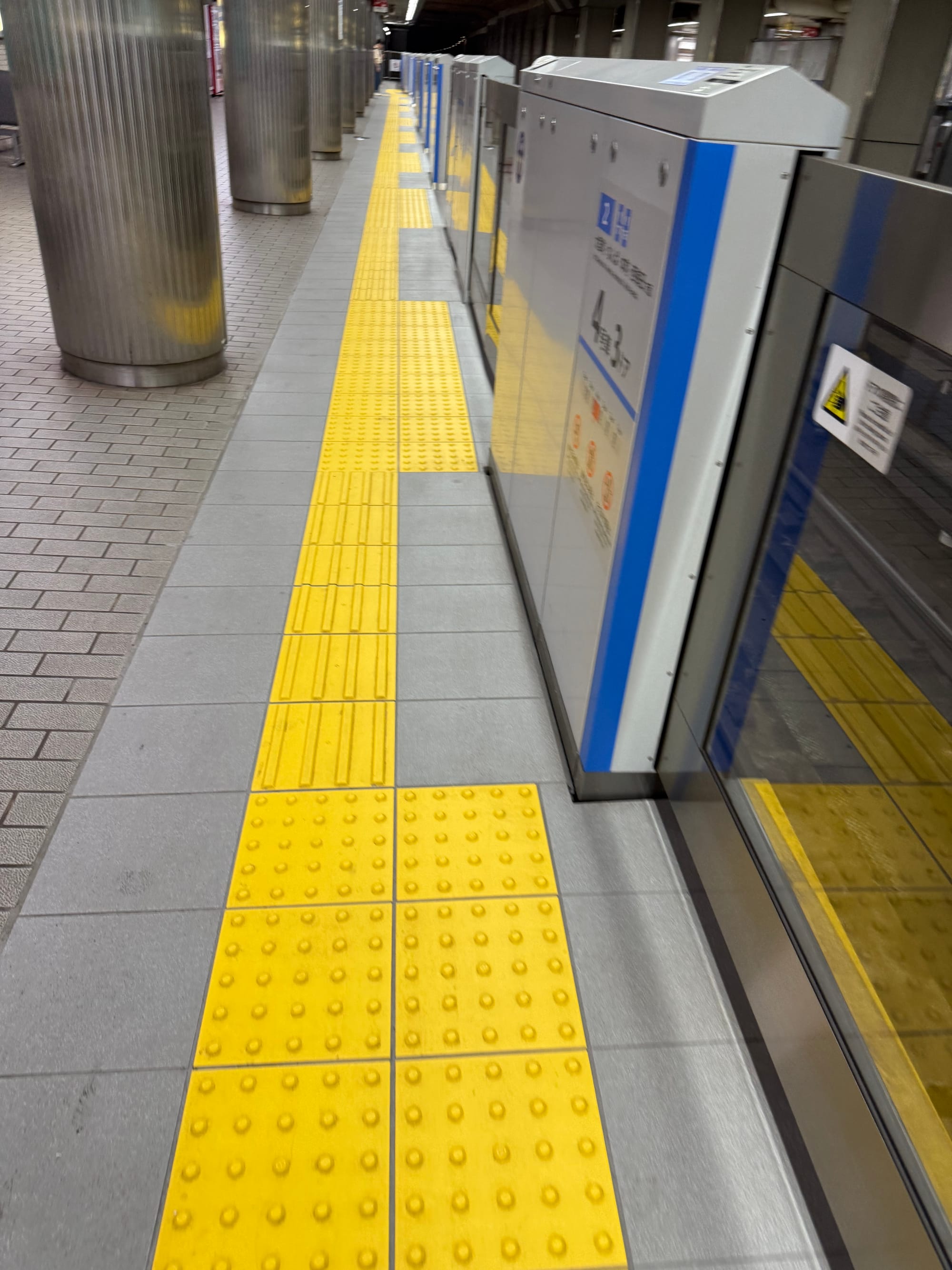 Platform screen doors and yellow tactile paving at an underground station in Osaka, showing accessibility features designed to guide and protect passengers.