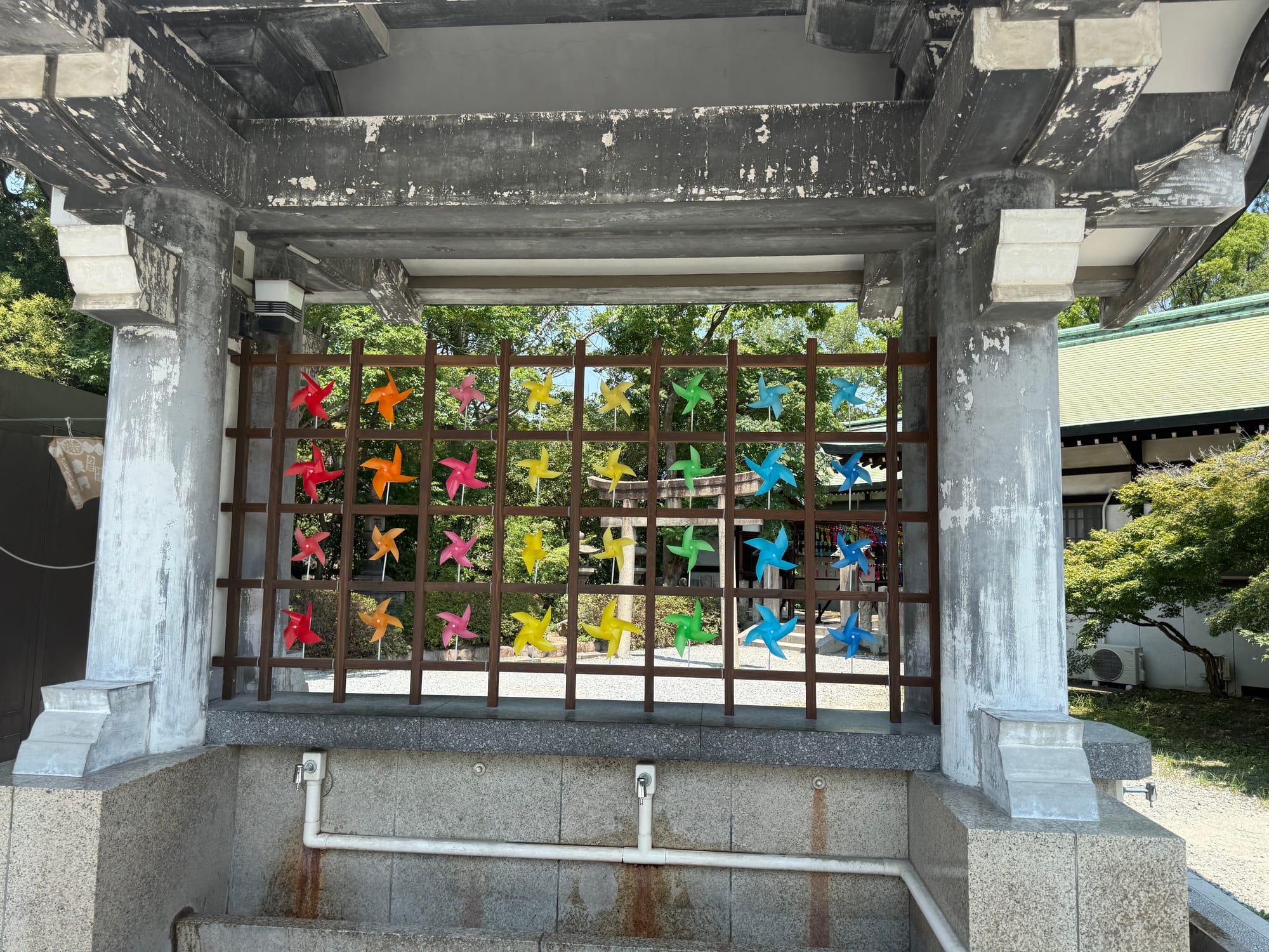 Colourful pinwheels displayed on a wooden frame at Hokoku Shrine in Osaka Castle Park, with the shrine grounds and a torii gate visible in the background.