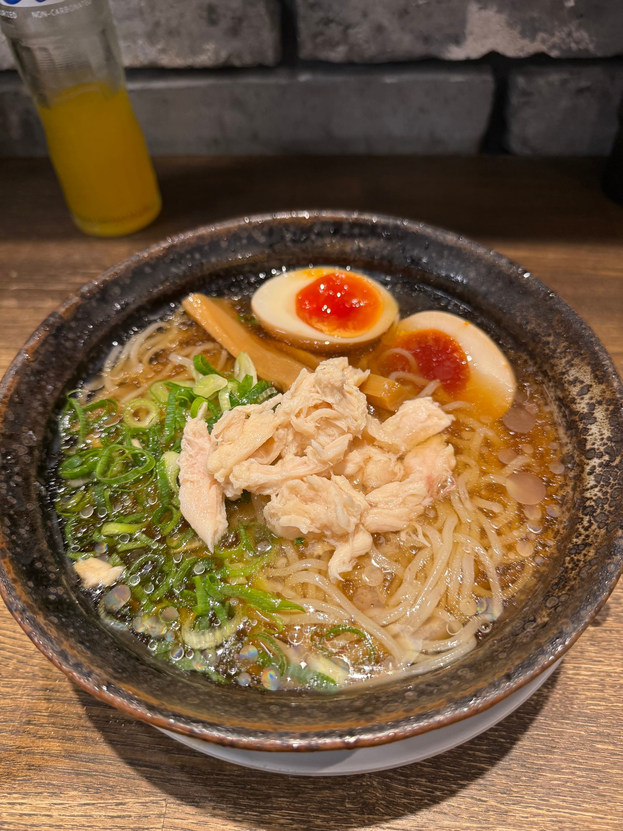 Bowl of chilled shoyu ramen topped with shredded chicken, spring onions, bamboo shoots and marinated soft-boiled eggs, served at a counter in a Japanese restaurant.