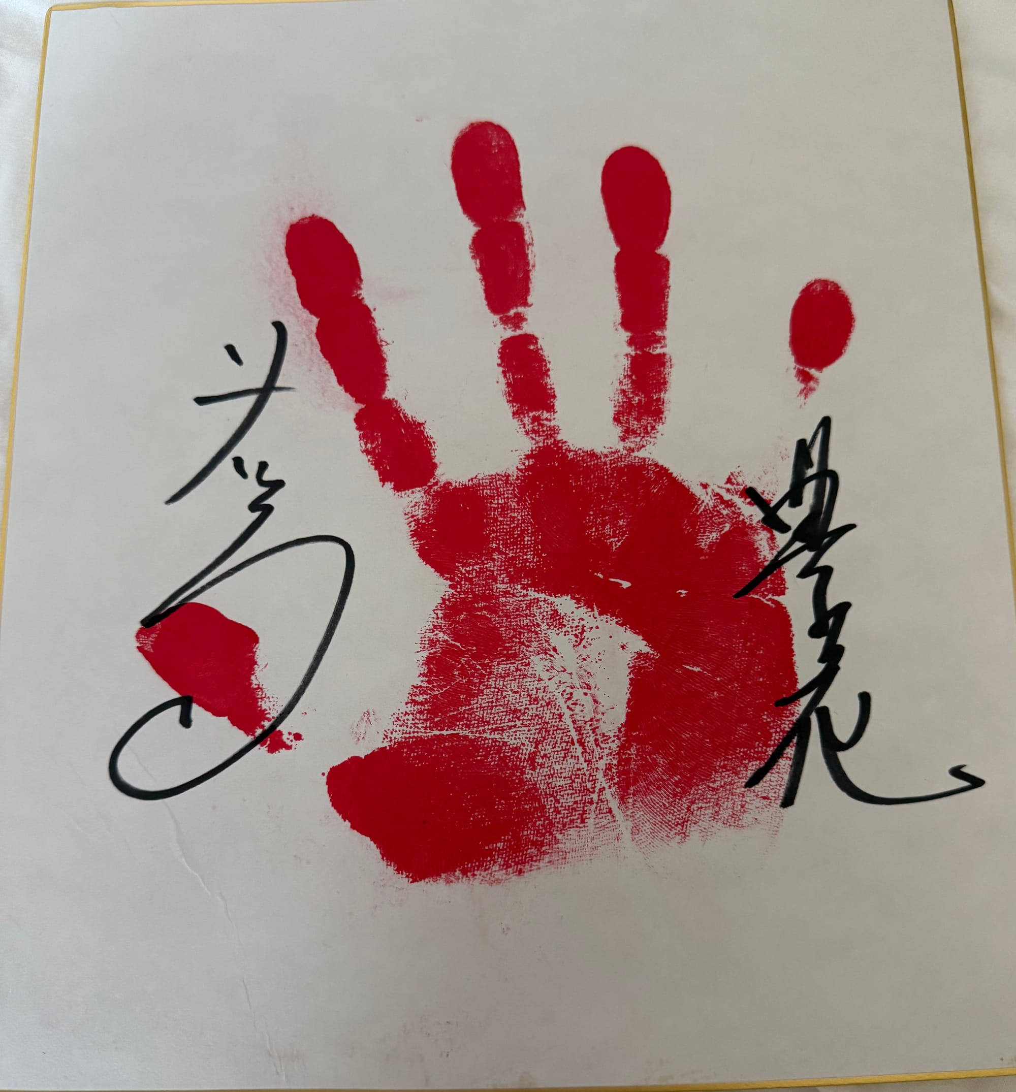 Red handprint on a shikishi autograph board, signed by two former sumo wrestlers, presented as a souvenir following a sumo experience in Osaka.