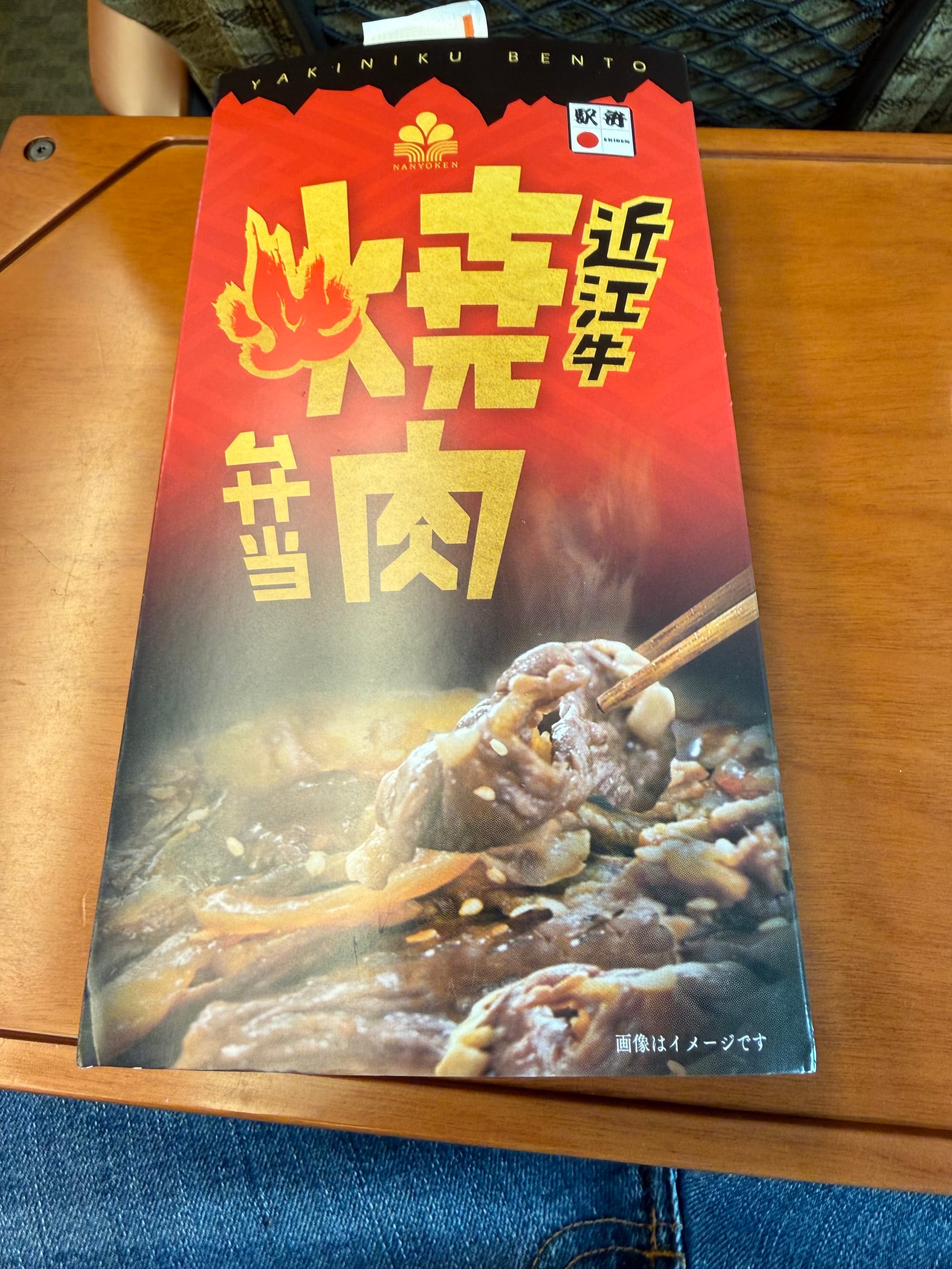Yakiniku bento box from Nan'yōken on board a Shinkansen, with packaging featuring grilled beef imagery and large Japanese characters on a red and black design.