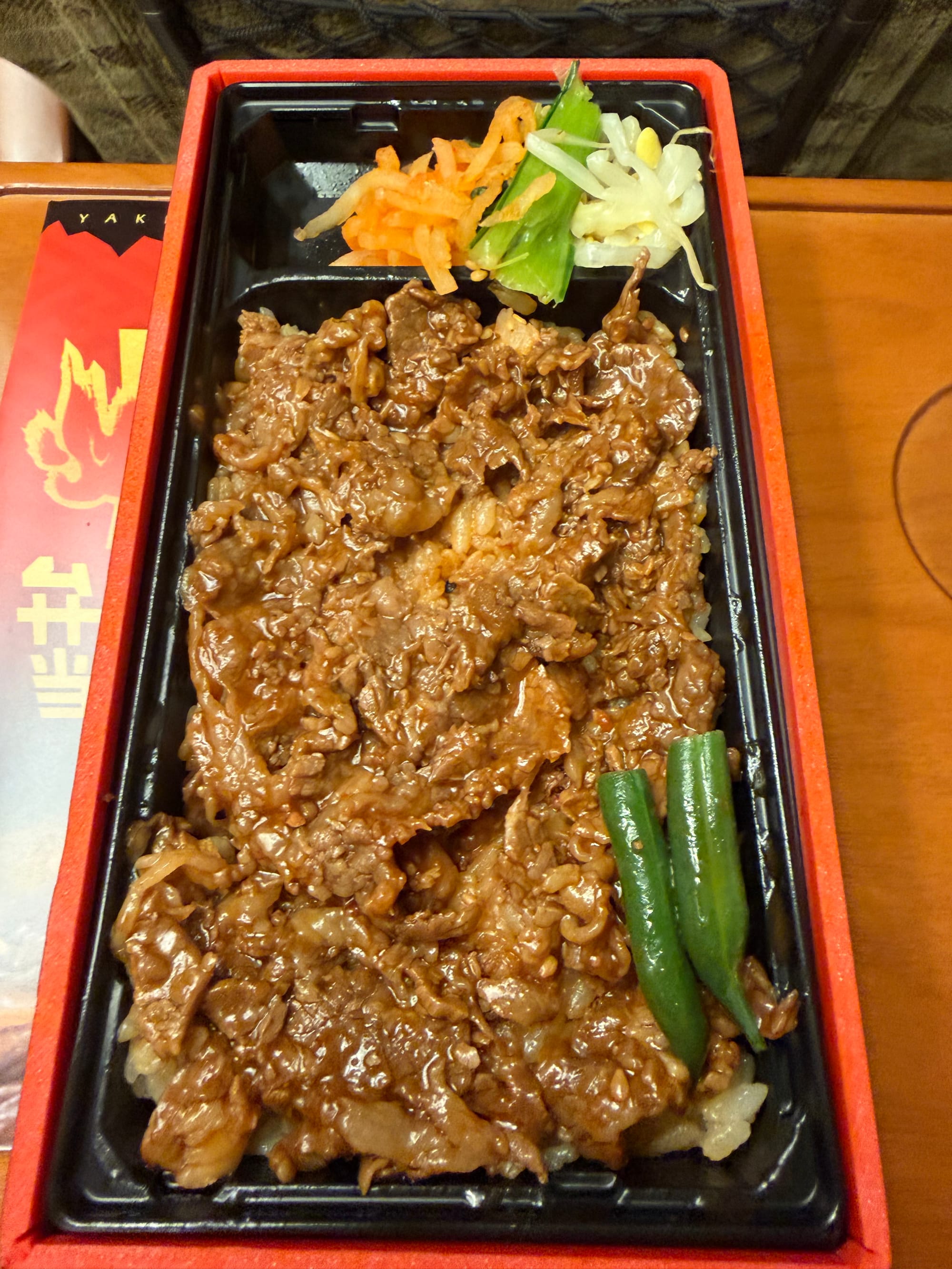 Yakiniku ekiben opened on board a Shinkansen, featuring sliced grilled beef over rice with green beans and pickled vegetables in a compartmented tray.