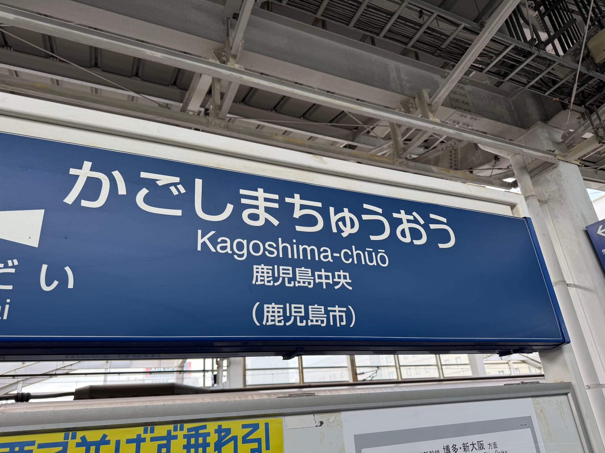 Station sign for Kagoshima-Chūō Station, displaying the station name in Japanese and English beneath the platform canopy at the southern terminus of the Kyushu Shinkansen.