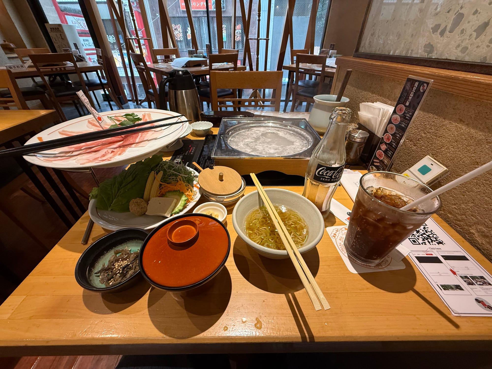 Kagoshima black pork shabu-shabu meal set on a restaurant table, featuring thinly sliced pork, vegetables, soba noodles, side dishes and a simmering hot pot.