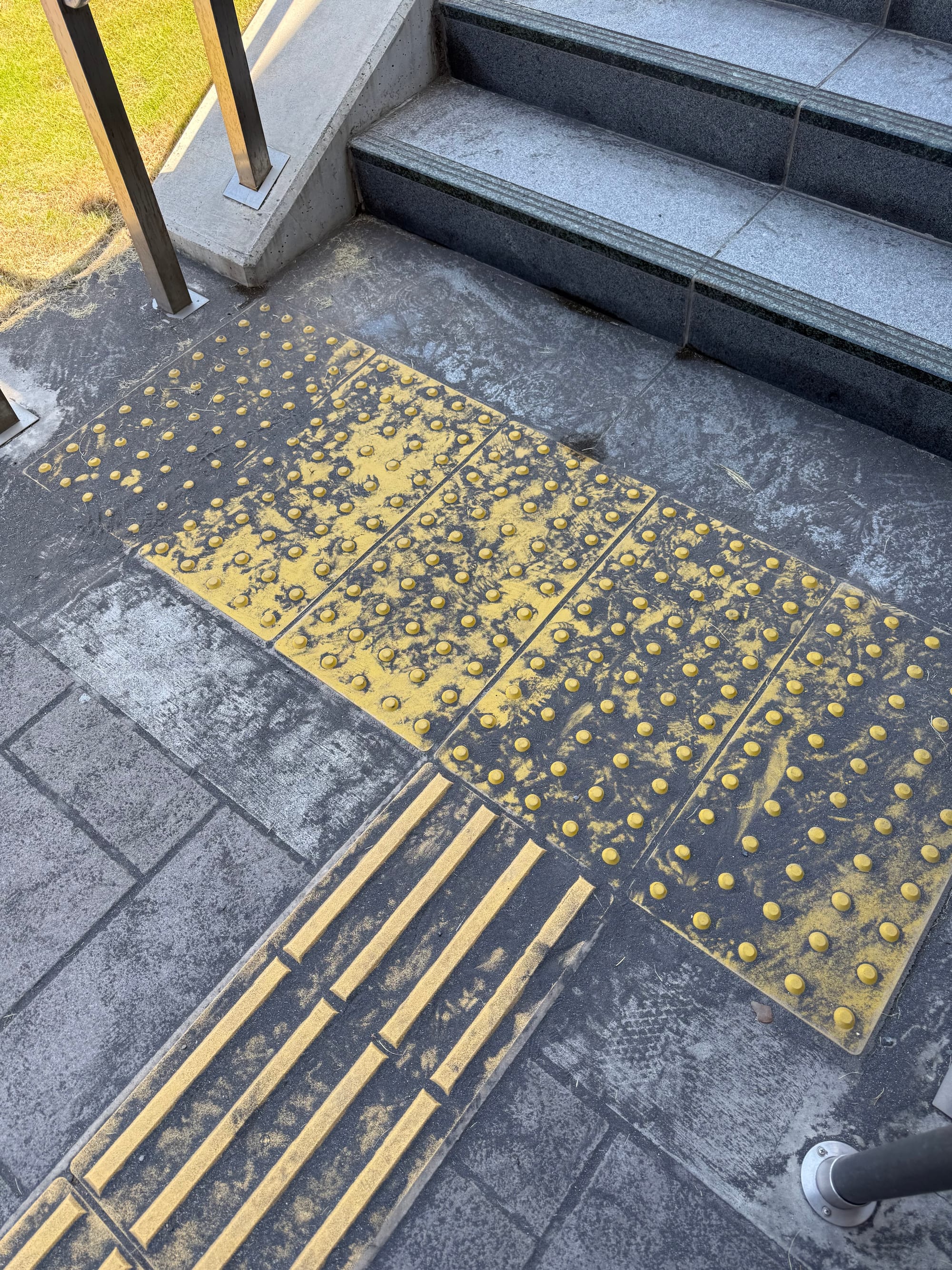Volcanic ash covers tactile paving and steps outside Sengan-en Station in Kagoshima, leaving a fine layer of grey dust across the pedestrian walkway.