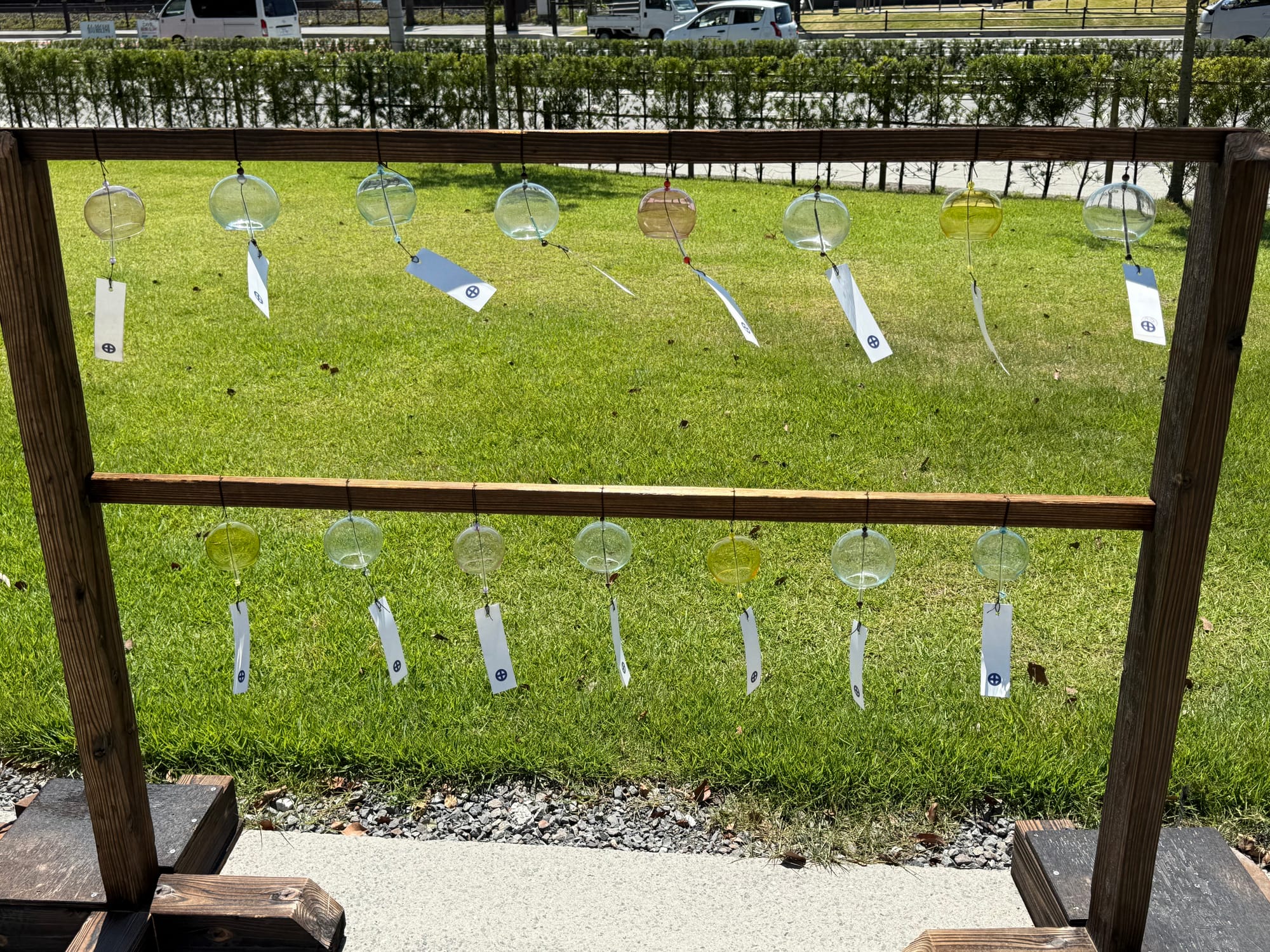 Glass wind chimes hang from a wooden display at Sengan-en, with paper strips fluttering in the breeze above a neatly kept lawn on a sunny summer day.