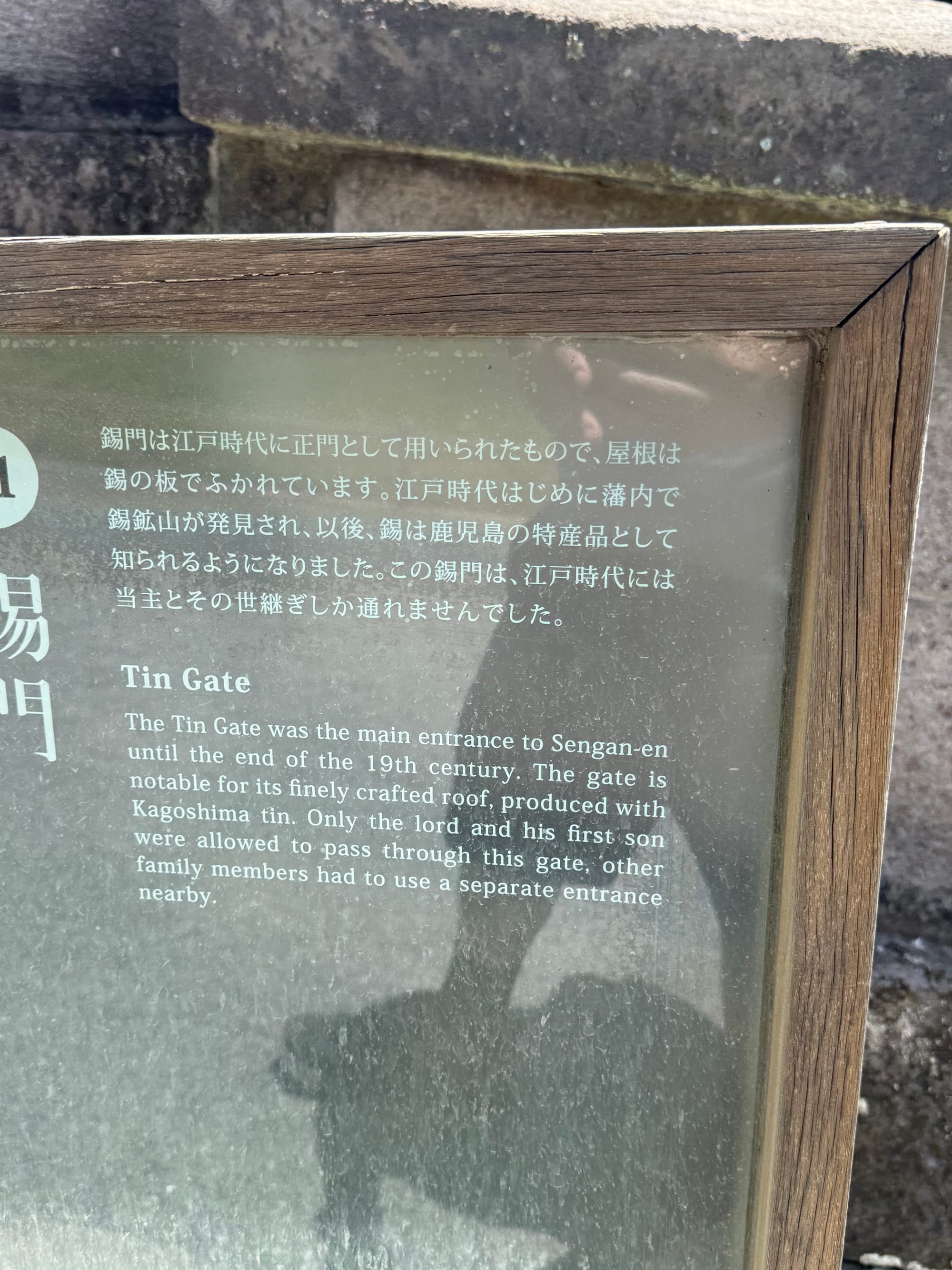 Information panel at Sengan-en describing the historic Tin Gate, explaining its role as the estate's main entrance and its distinctive roof crafted using Kagoshima tin.
