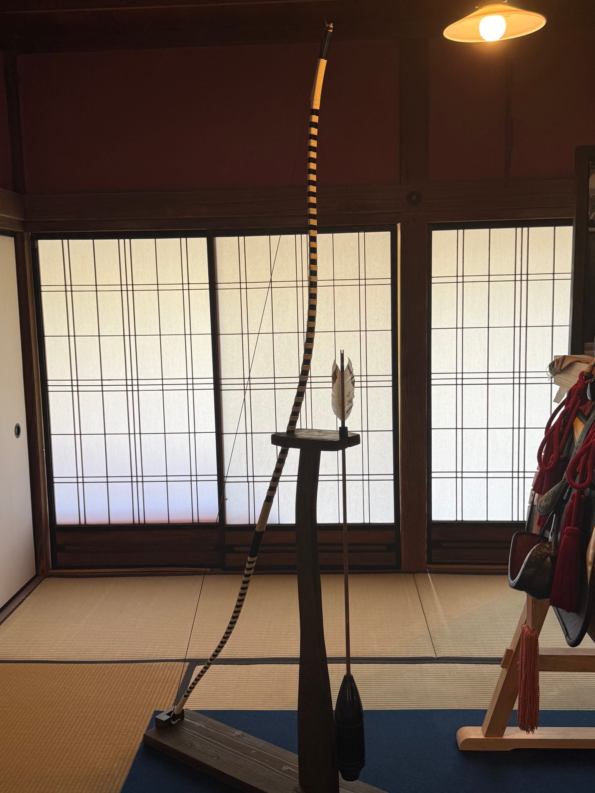 Traditional Japanese longbow (yumi) and arrow displayed on a stand inside a tatami-floored room at Sengan-en, with shoji screens and samurai equipment nearby.