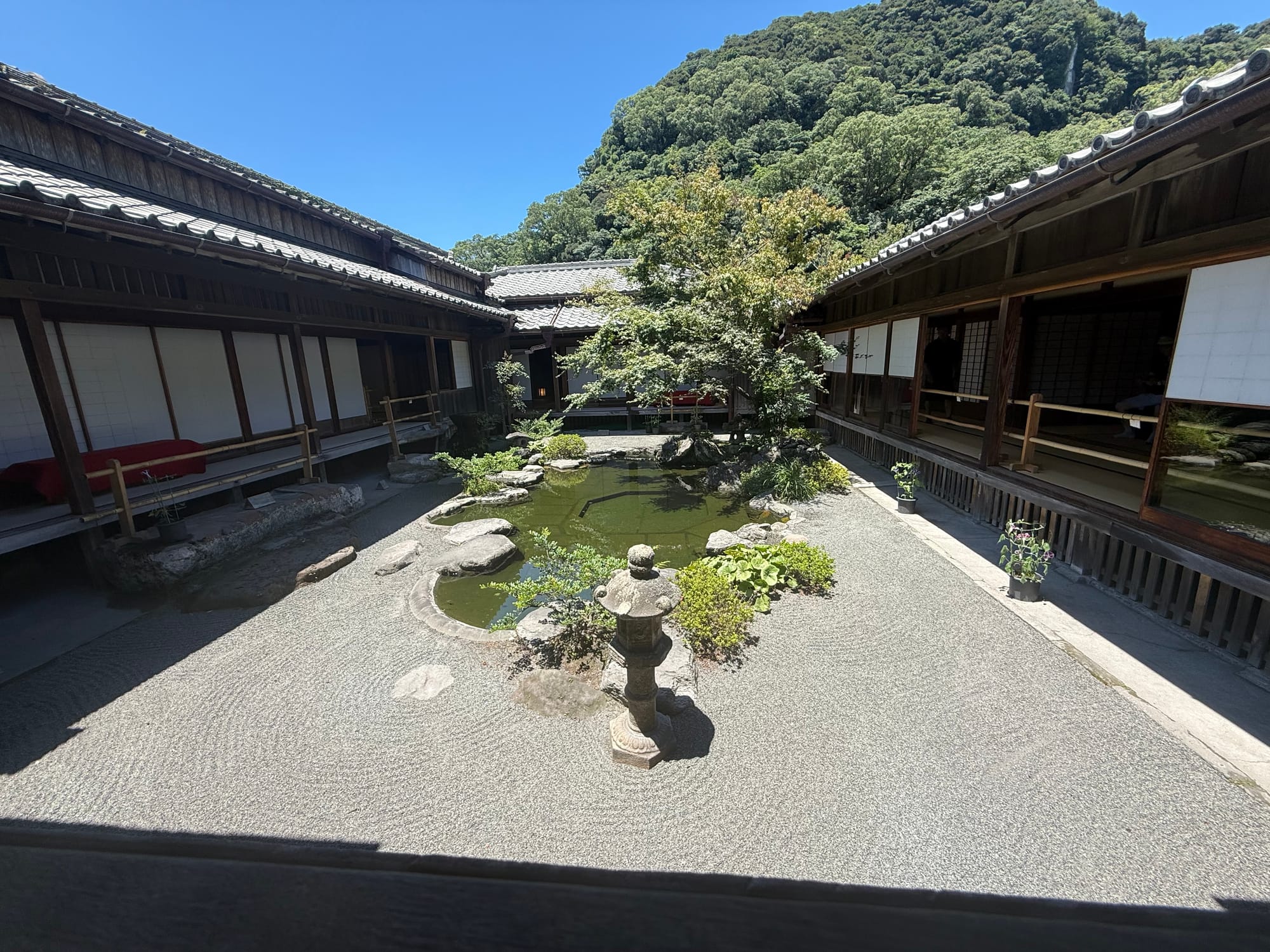 Traditional Japanese courtyard garden at Sengan-en, featuring a pond, stone lantern, gravel landscaping and wooden buildings set against forested hills.