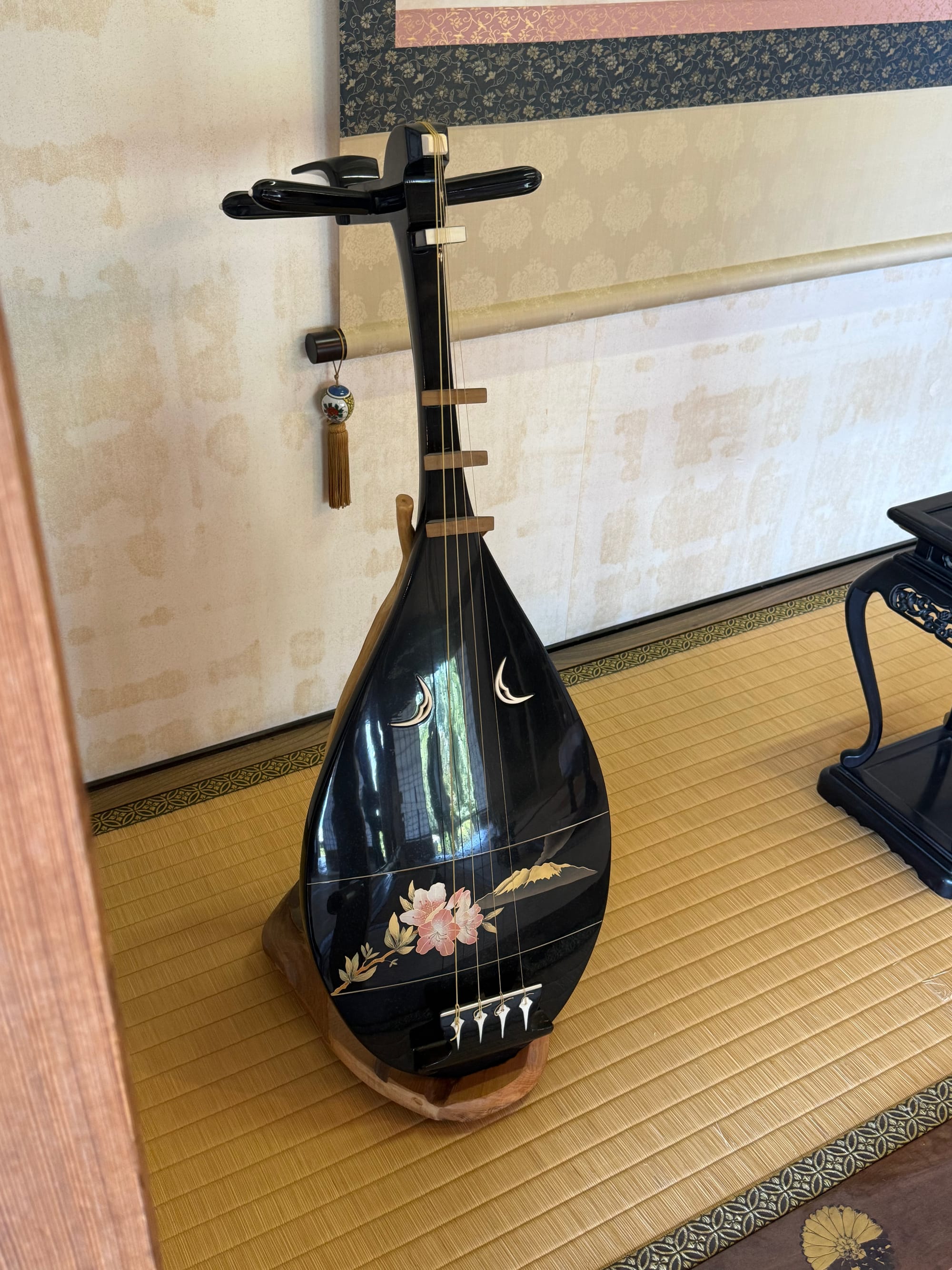 Traditional Japanese biwa lute displayed on tatami flooring at Sengan-en, featuring black lacquer, floral decoration and ivory-coloured fittings in a historic room.