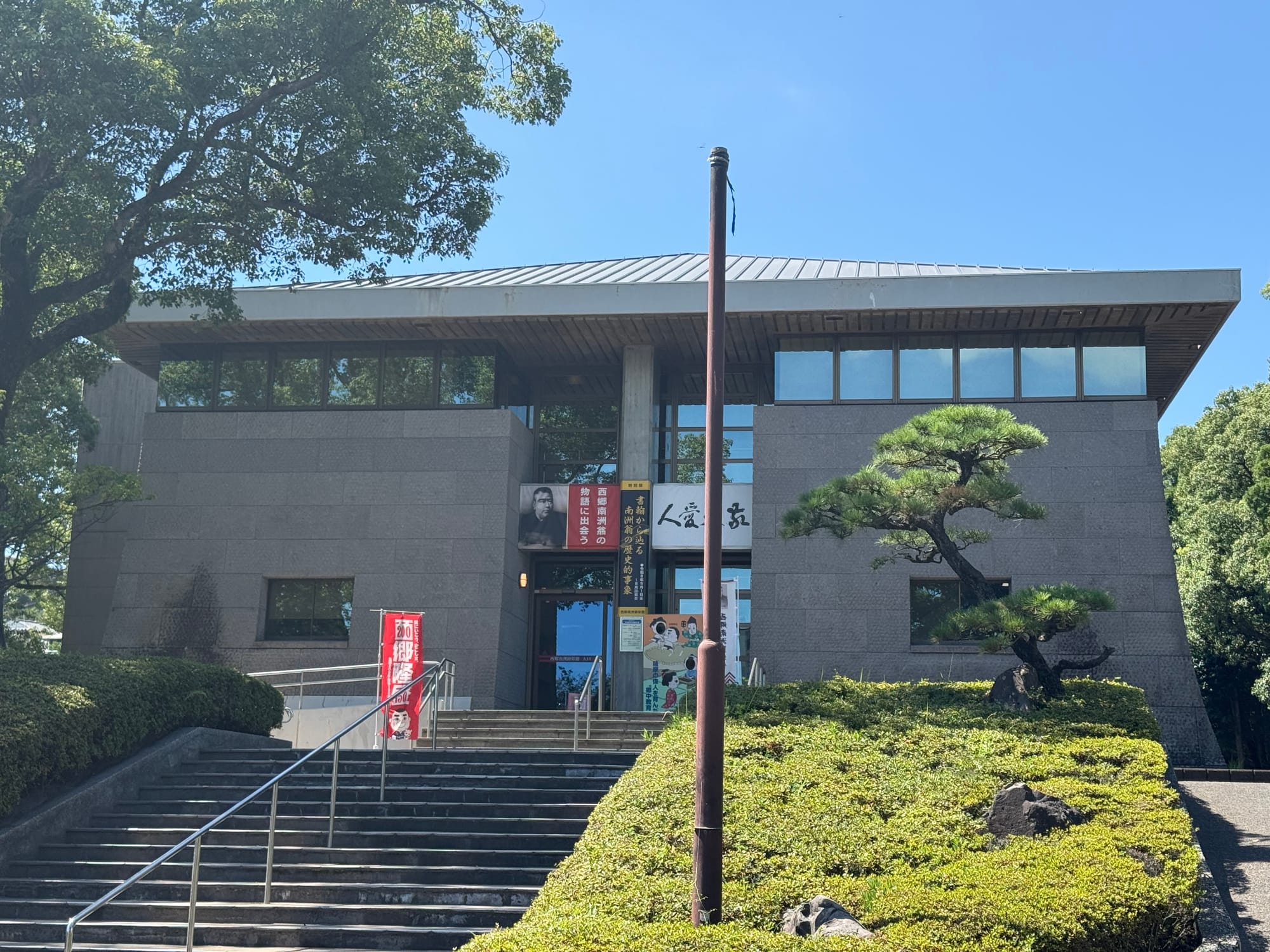 Saigo Nanshu Memorial Museum in Kagoshima, a modern museum building surrounded by trees and landscaped gardens, with steps leading to the main entrance.