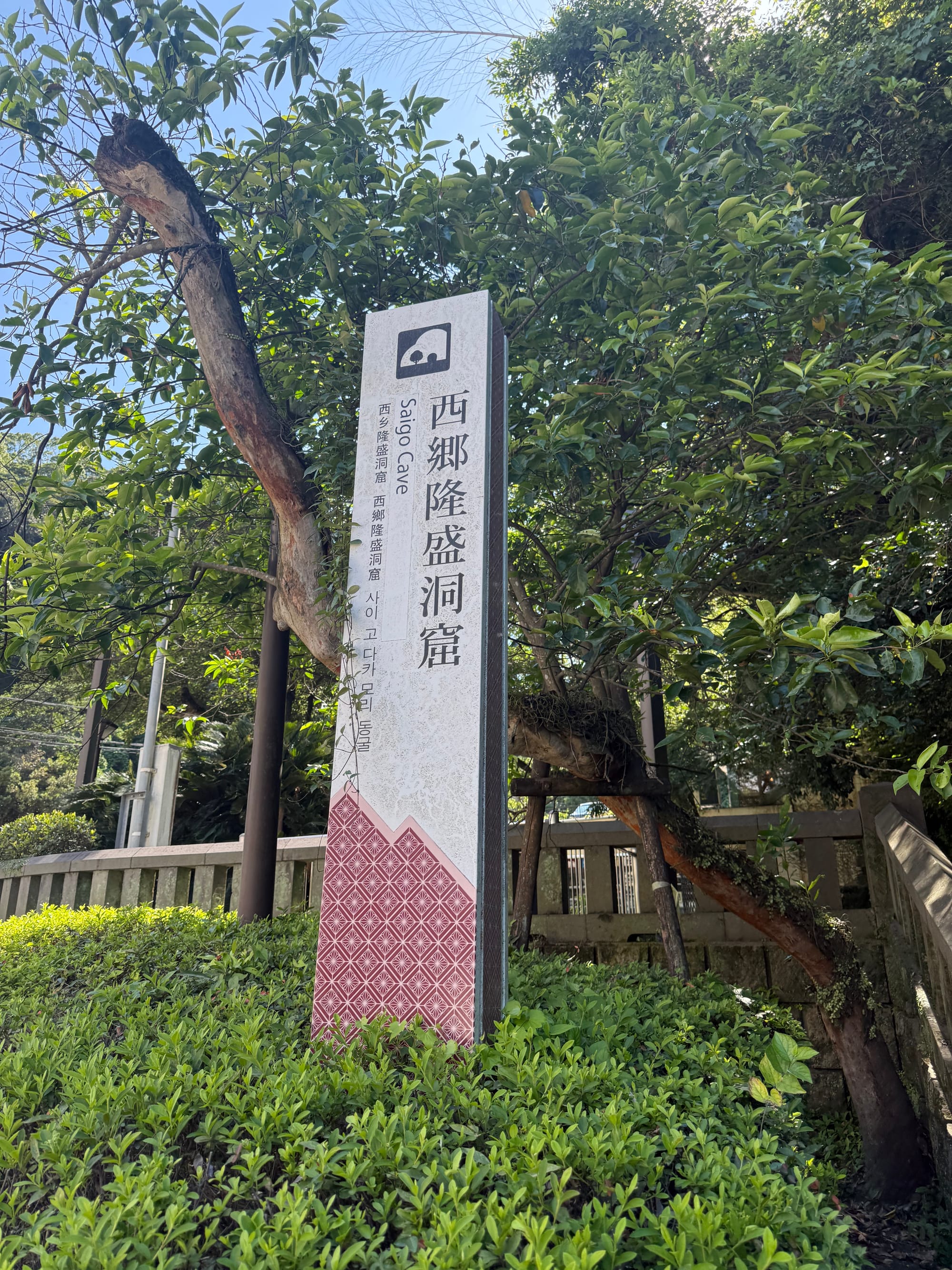 Sign marking Saigō Cave in Kagoshima, surrounded by trees and shrubs, indicating the historic site where Saigō Takamori spent his final days during the Satsuma Rebellion.