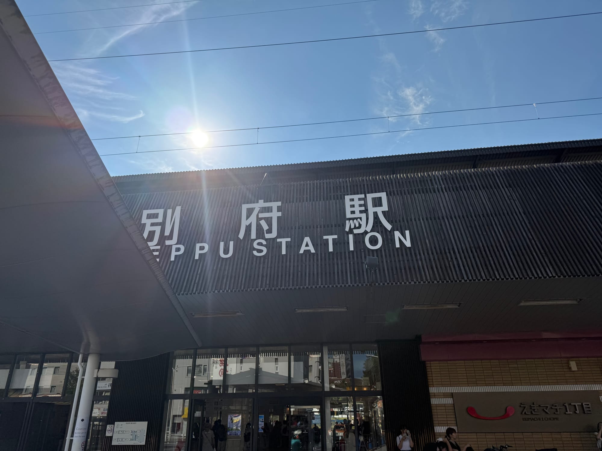 Exterior of Beppu Station in Ōita Prefecture, featuring large station signage, a modern wooden façade and bright sunshine overhead on a clear summer day.