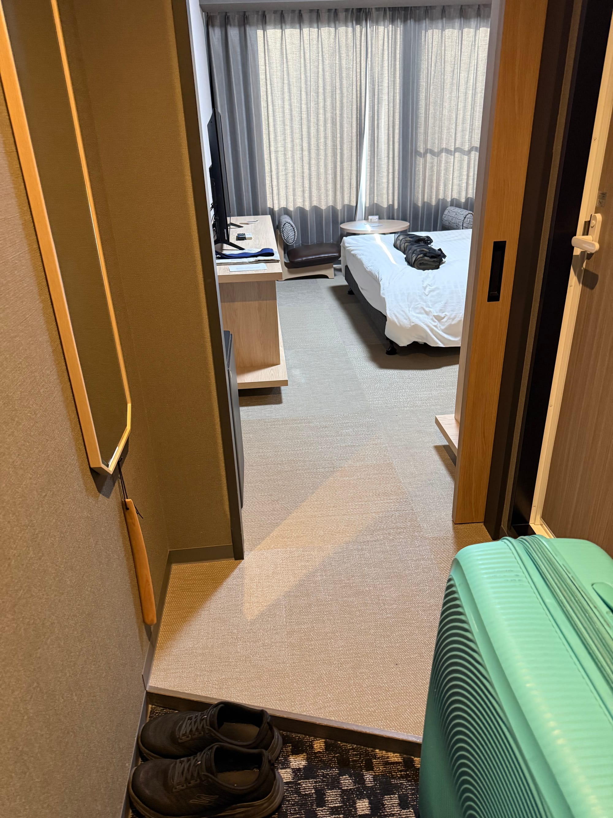Hotel room at Grandvrio Hotel Beppu Bay Wakura, viewed from the entrance, featuring a bed, desk, seating area, large window and a turquoise suitcase.