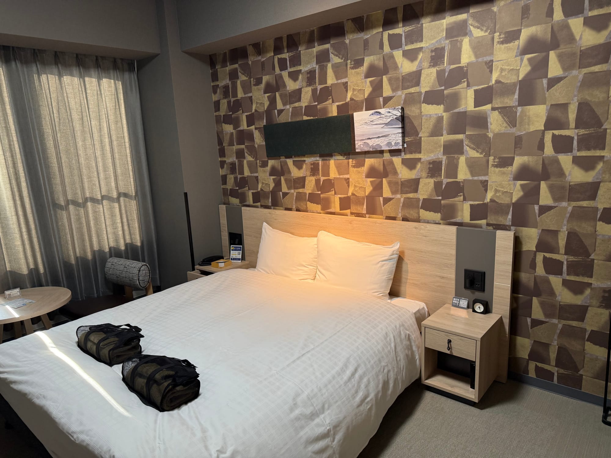 Double room at Grandvrio Hotel Beppu Bay Wakura, featuring a large bed, patterned feature wall, bedside tables, seating area and a window with drawn curtains.