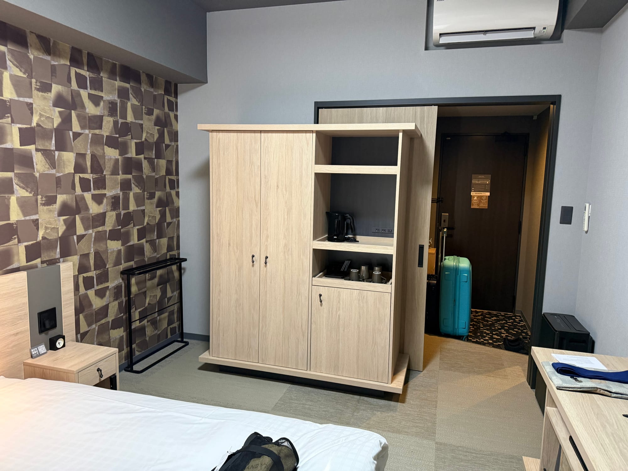 Modern hotel room at Grandvrio Hotel Beppu Bay Wakura, featuring a large bed, wooden storage unit, tea-making facilities, desk area and luggage near the entrance.