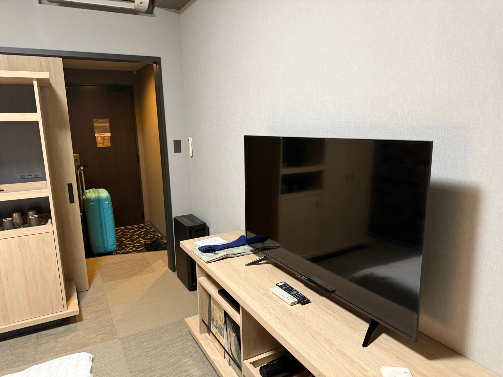 Large television and storage unit inside a room at Grandvrio Hotel Beppu Bay Wakura, with tea-making facilities, luggage and the entrance area visible in the background.