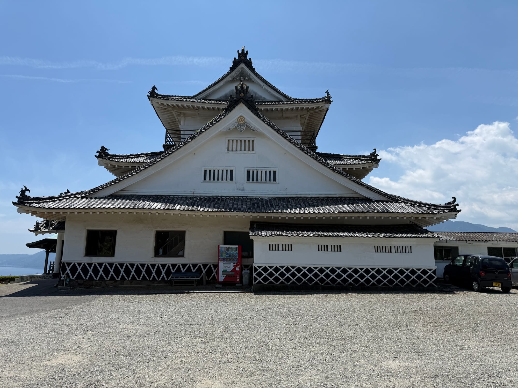 Kifune Castle overlooking Lake Shidaka near Beppu, featuring white plaster walls, black tiled roofs and a traditional multi-tiered castle keep beneath a clear blue sky.