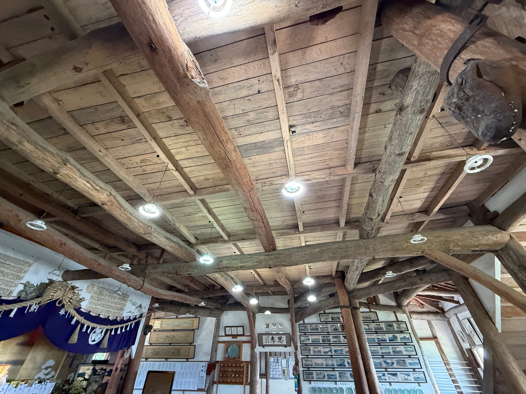 Interior of Kifune Castle featuring heavy timber beams, wooden pillars, historic displays, framed photographs and exhibits arranged beneath a traditional wooden ceiling.