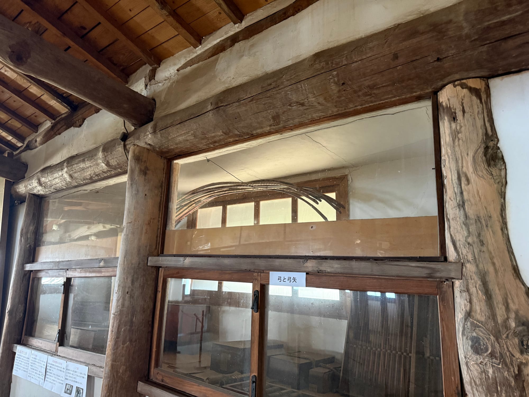 Display case inside Kifune Castle containing traditional Japanese bows and arrows, set within a historic timber-framed interior with exposed wooden beams and pillars.