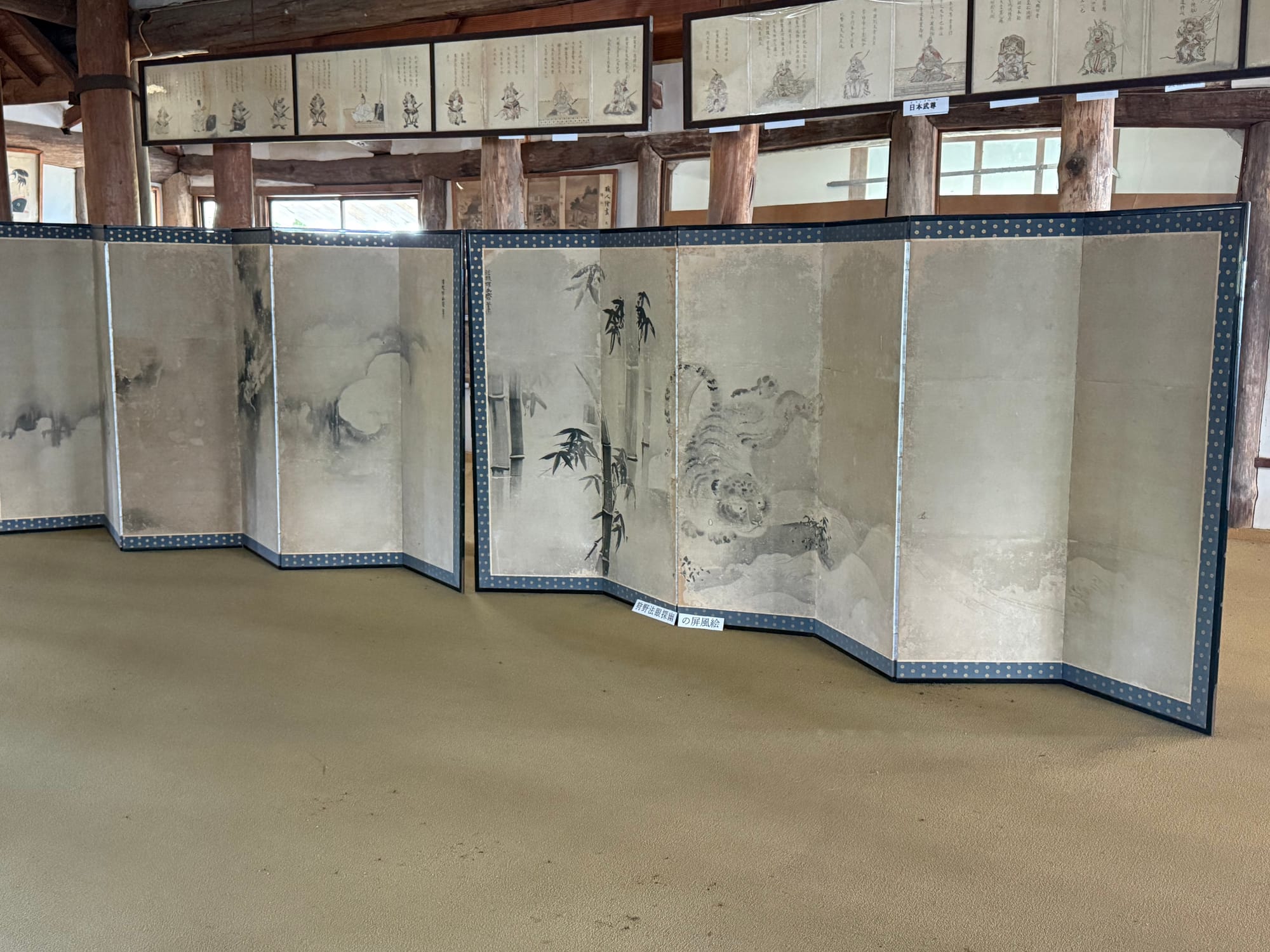 Traditional Japanese folding screens displayed inside Kifune Castle, featuring ink paintings of a tiger and bamboo, surrounded by exposed timber beams and historic interiors.
