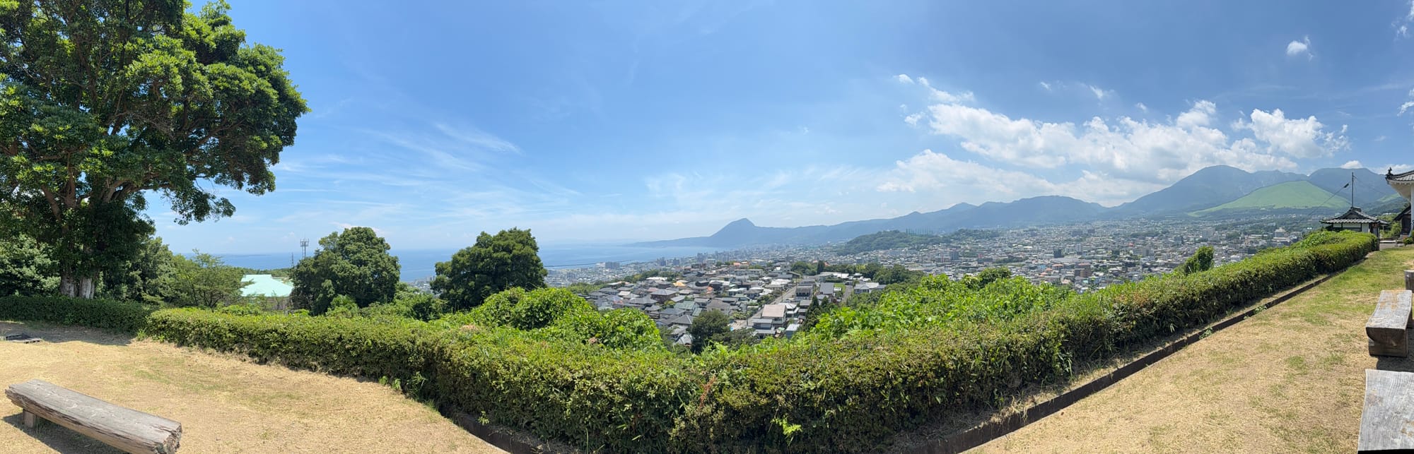 Panoramic view from Kifune Castle overlooking Beppu, with Beppu Bay, residential neighbourhoods, green hills and mountains stretching beneath a clear summer sky.