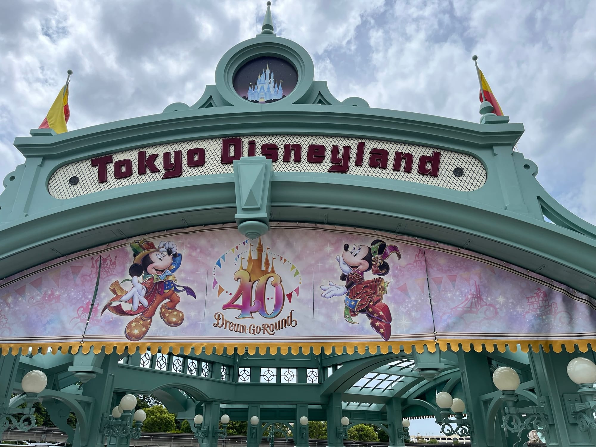 Tokyo Disneyland entrance arch featuring the 40th Dream-Go-Round anniversary banner with Mickey Mouse and Minnie Mouse beneath decorative pastel architecture and cloudy skies.