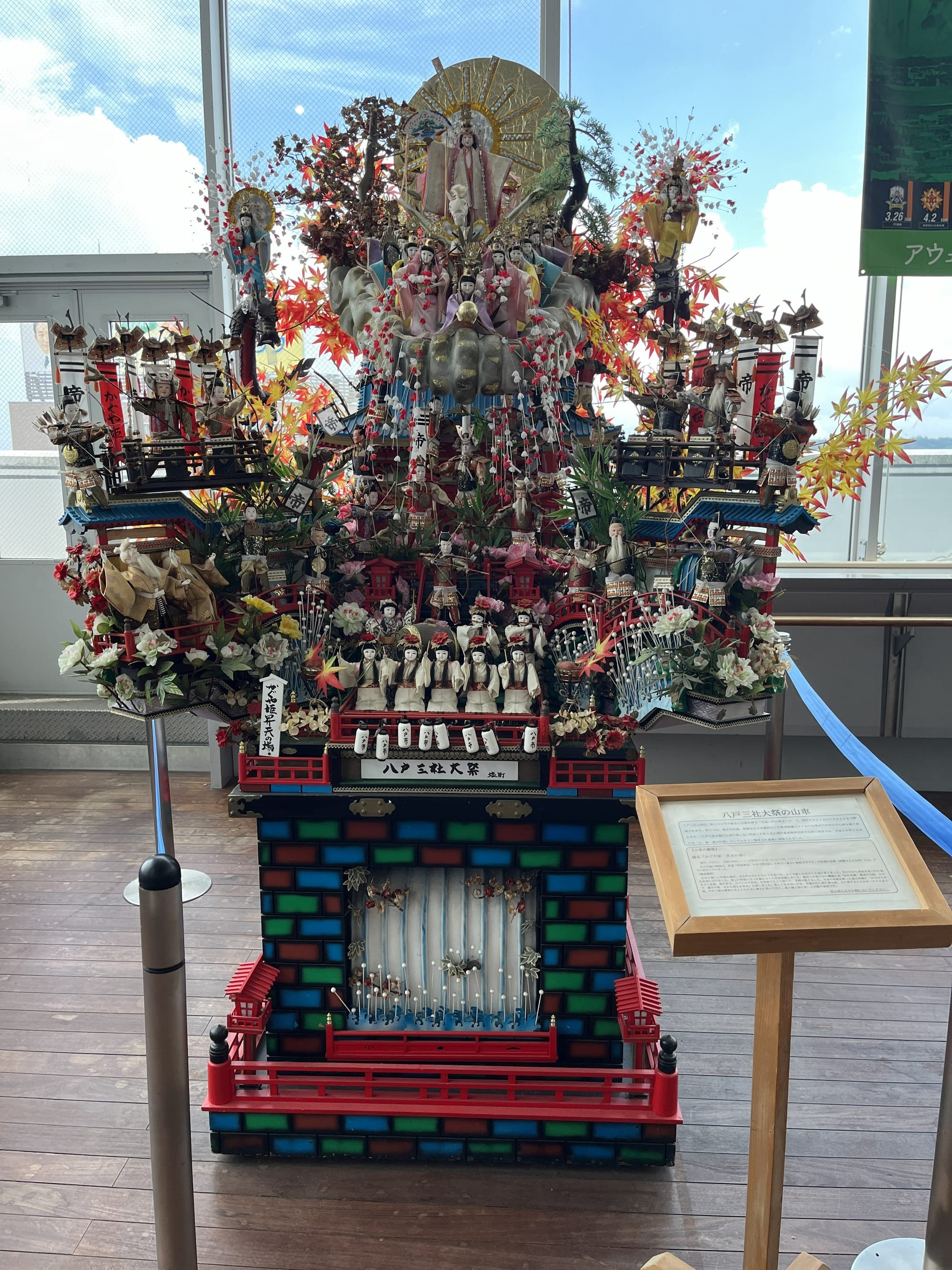 Elaborate miniature festival float on display at Hachinohe Station, decorated with figures, lanterns, flowers and traditional Japanese motifs linked to local celebrations.