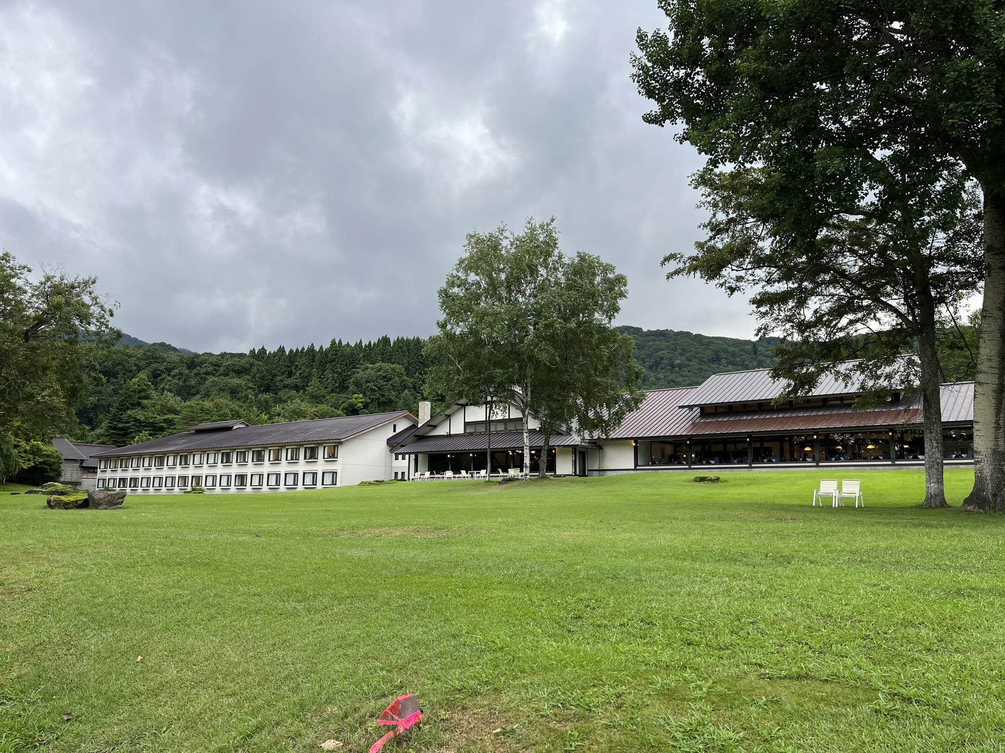 Towada Prince Hotel beside Lake Towada, surrounded by lawns and forested hills, beneath dark rain clouds gathering over northern Japan.