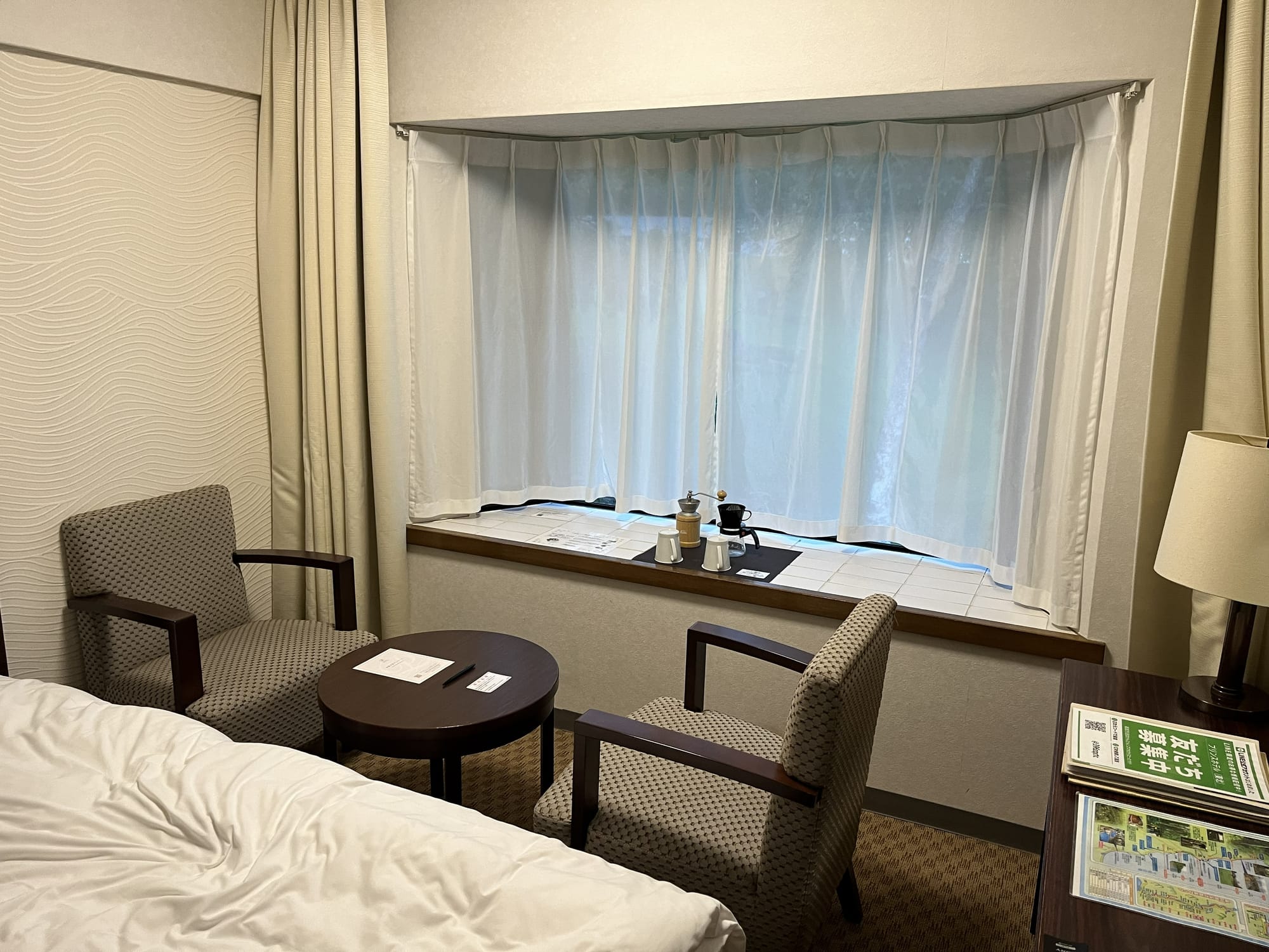 Seating area inside a room at Towada Prince Hotel, featuring armchairs, a small table and tea-making facilities beside a large window overlooking the grounds.