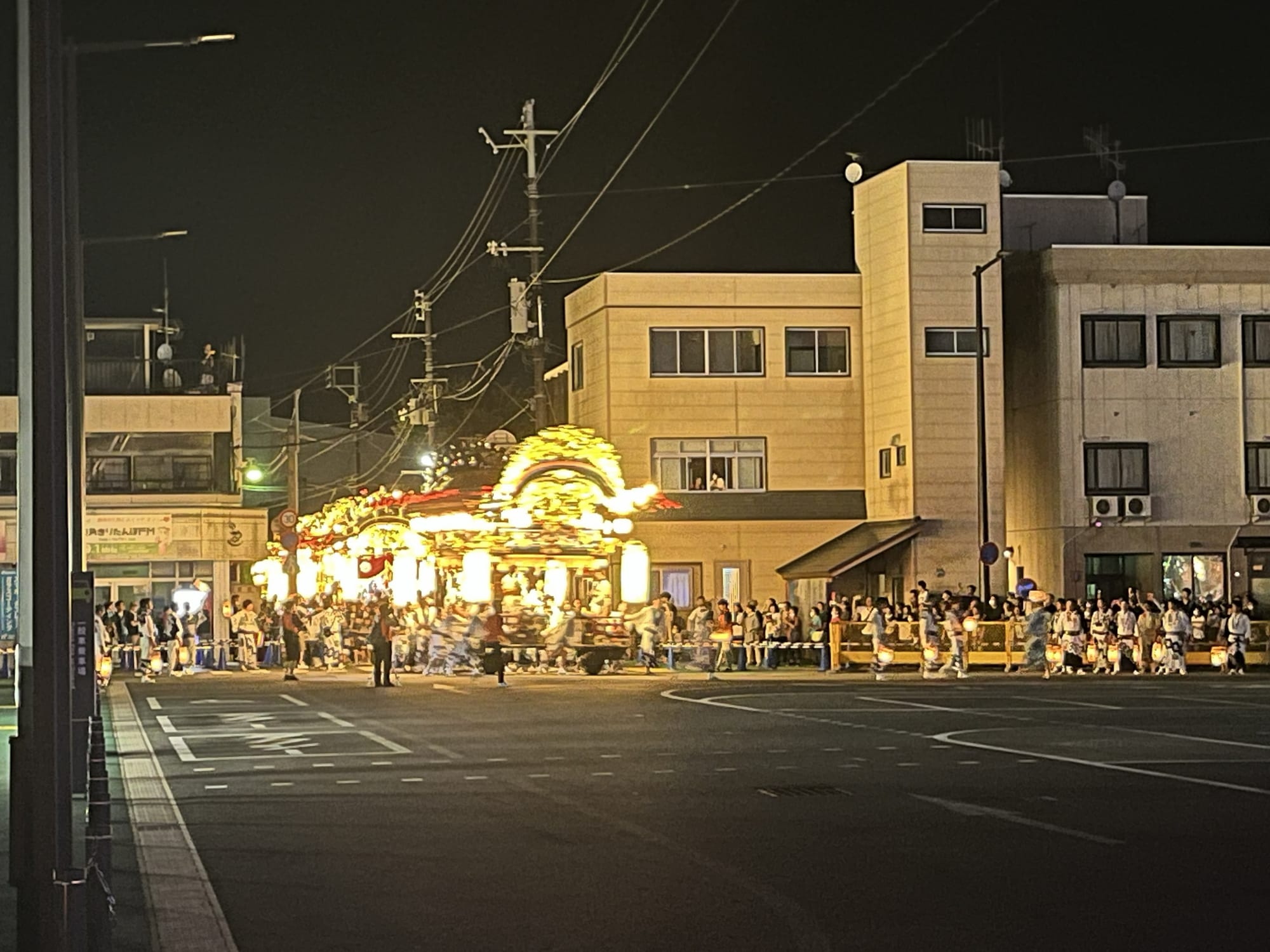 Illuminated festival float covered in lanterns travels through the streets of Kazuno at night, surrounded by spectators and participants in traditional festival dress.