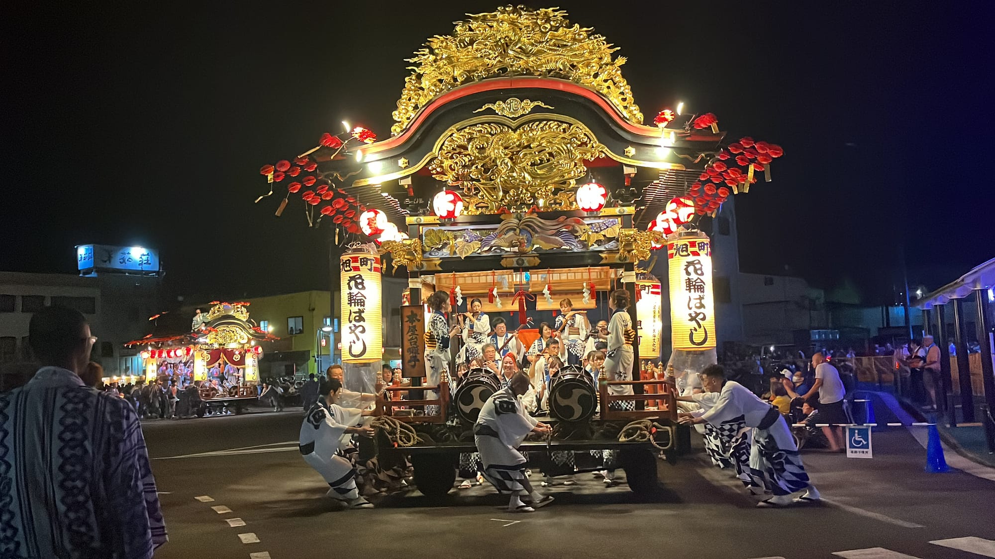 Illuminated festival floats decorated with lanterns and gold carvings move through the streets of Kazuno at night, guided by participants in traditional dress.