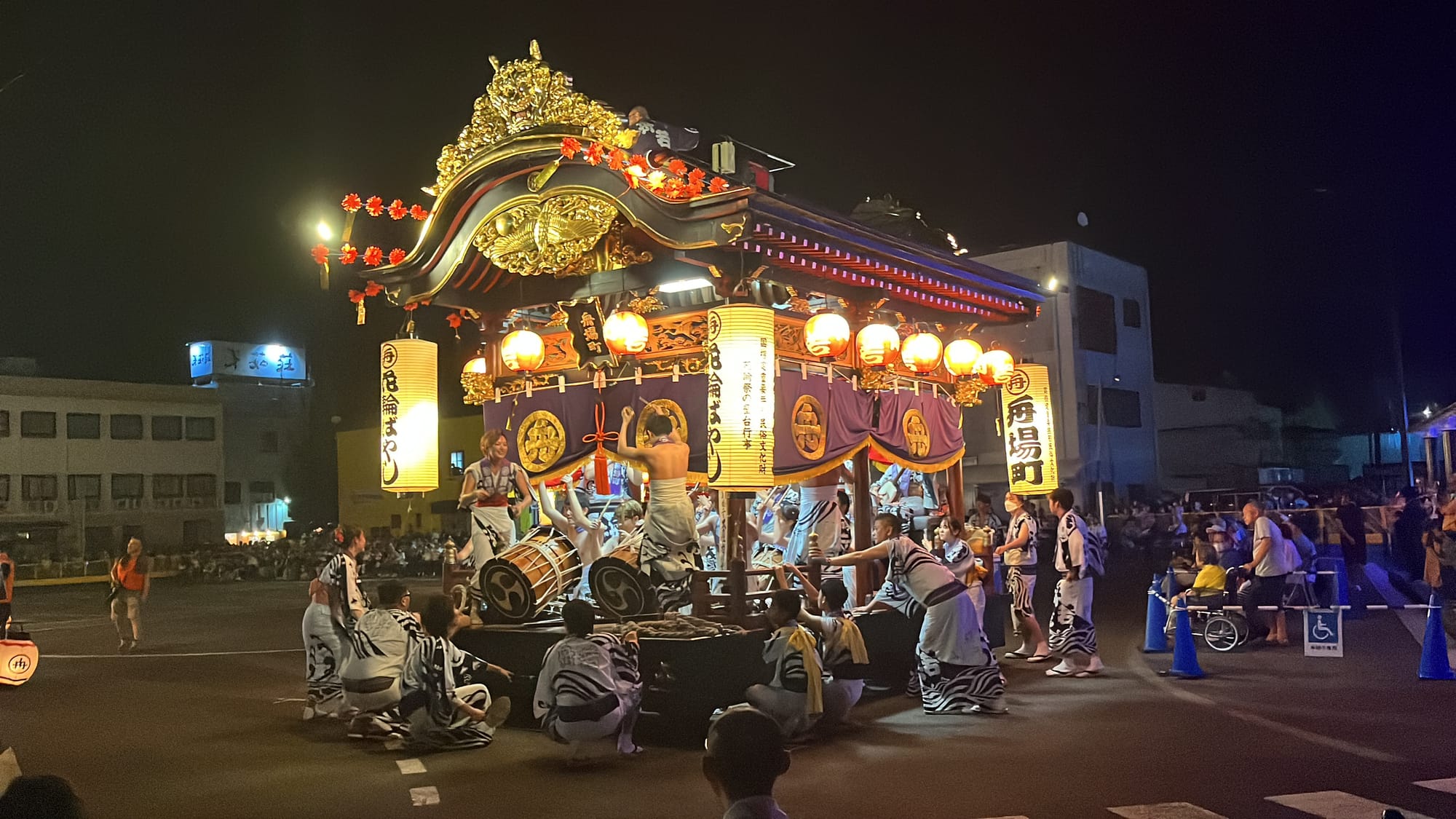 Lantern-lit festival float in Kazuno decorated with ornate gold carvings, surrounded by drummers and participants in traditional dress during a night-time procession.
