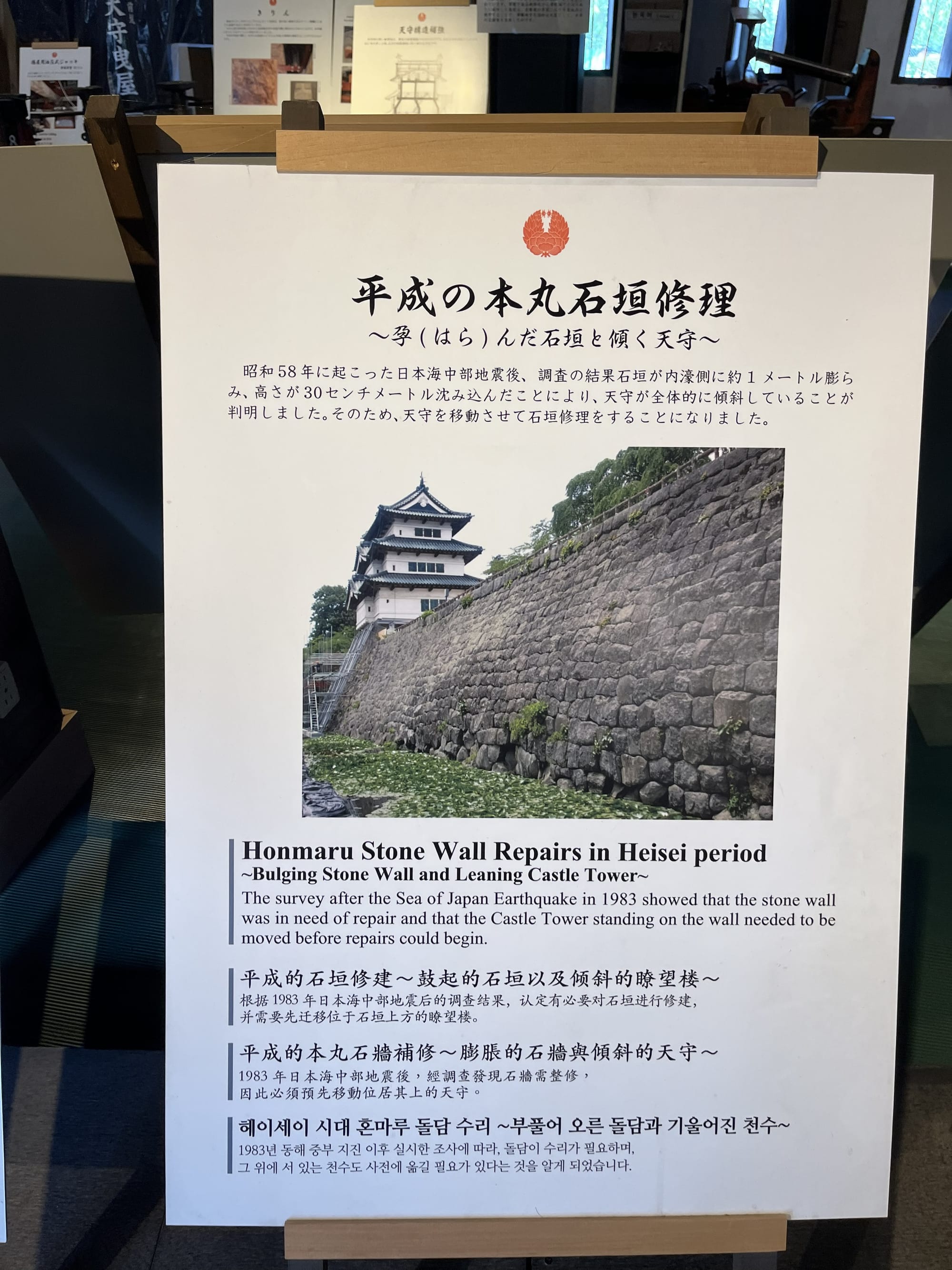 Information board inside Hirosaki Castle explaining the Heisei-era repairs to the castle's stone walls and keep, with photographs and text in Japanese and English.