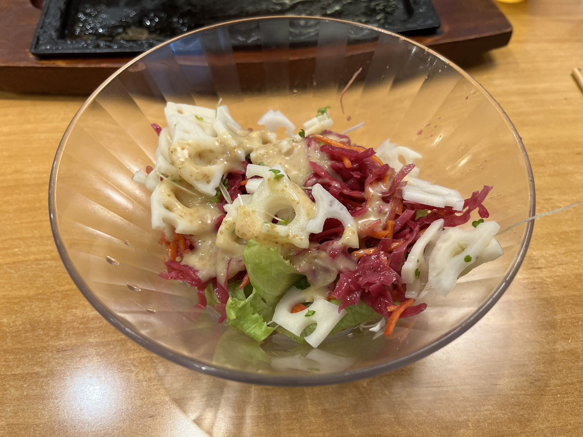 Mixed salad with lotus root slices, red cabbage, lettuce and carrot, served in a glass bowl with creamy dressing at a Japanese family restaurant.