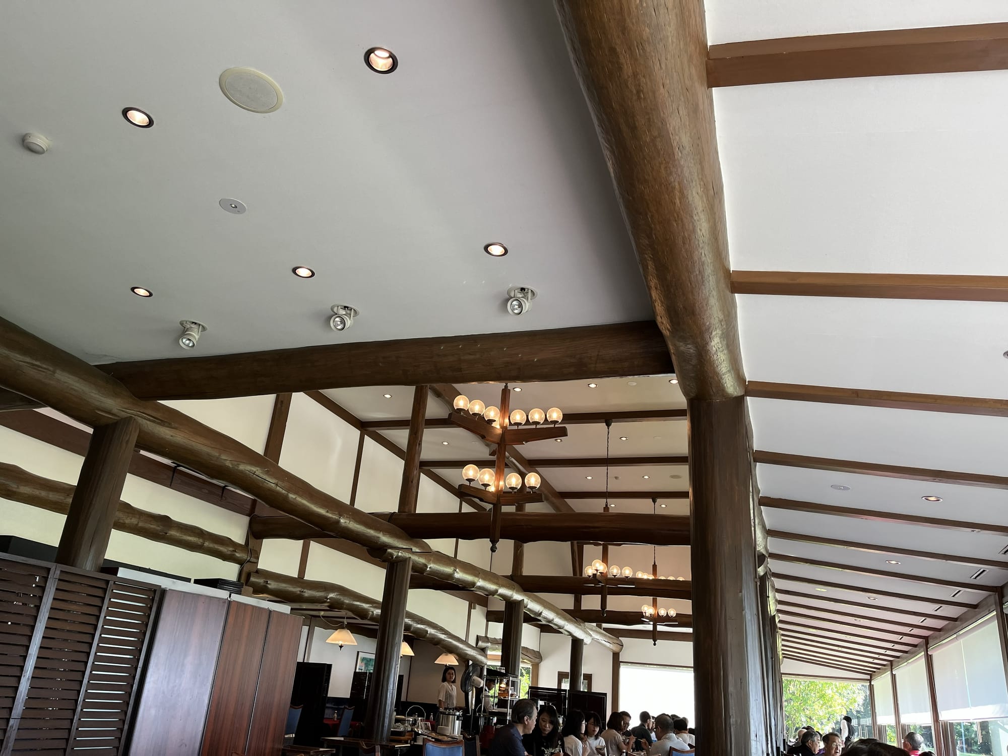 Interior of the Towada Prince Hotel restaurant, featuring exposed timber beams, hanging lights, dining tables and large windows overlooking Lake Towada.