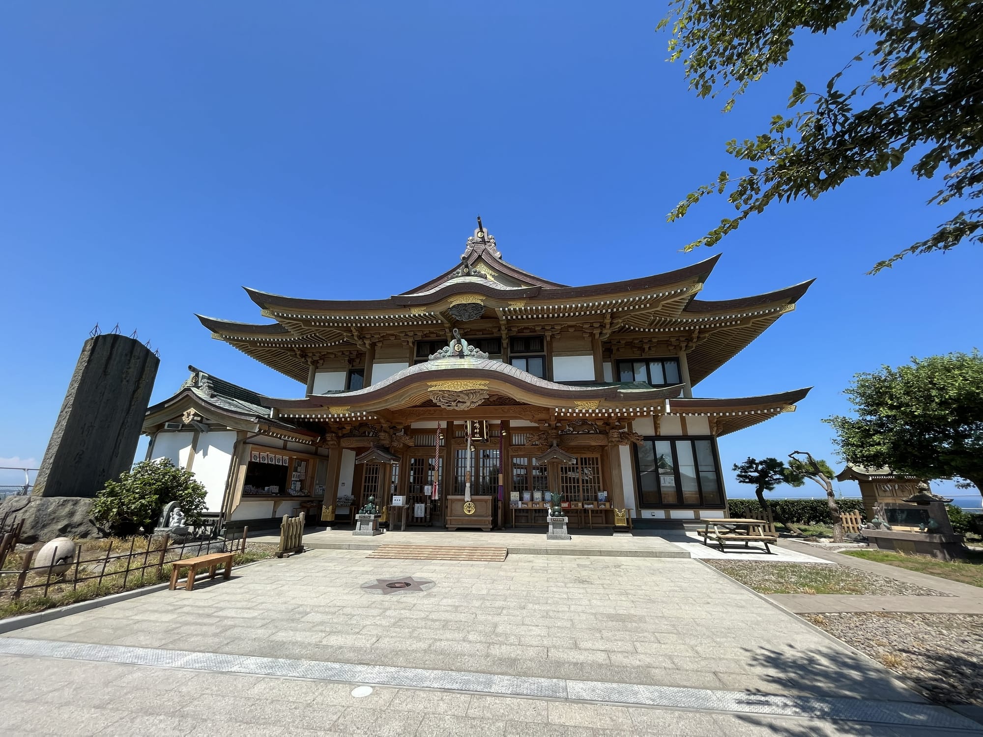 Main hall of Kabushima Shrine in Hachinohe, featuring ornate wooden architecture, curved rooflines and an open courtyard beneath a clear blue summer sky.
