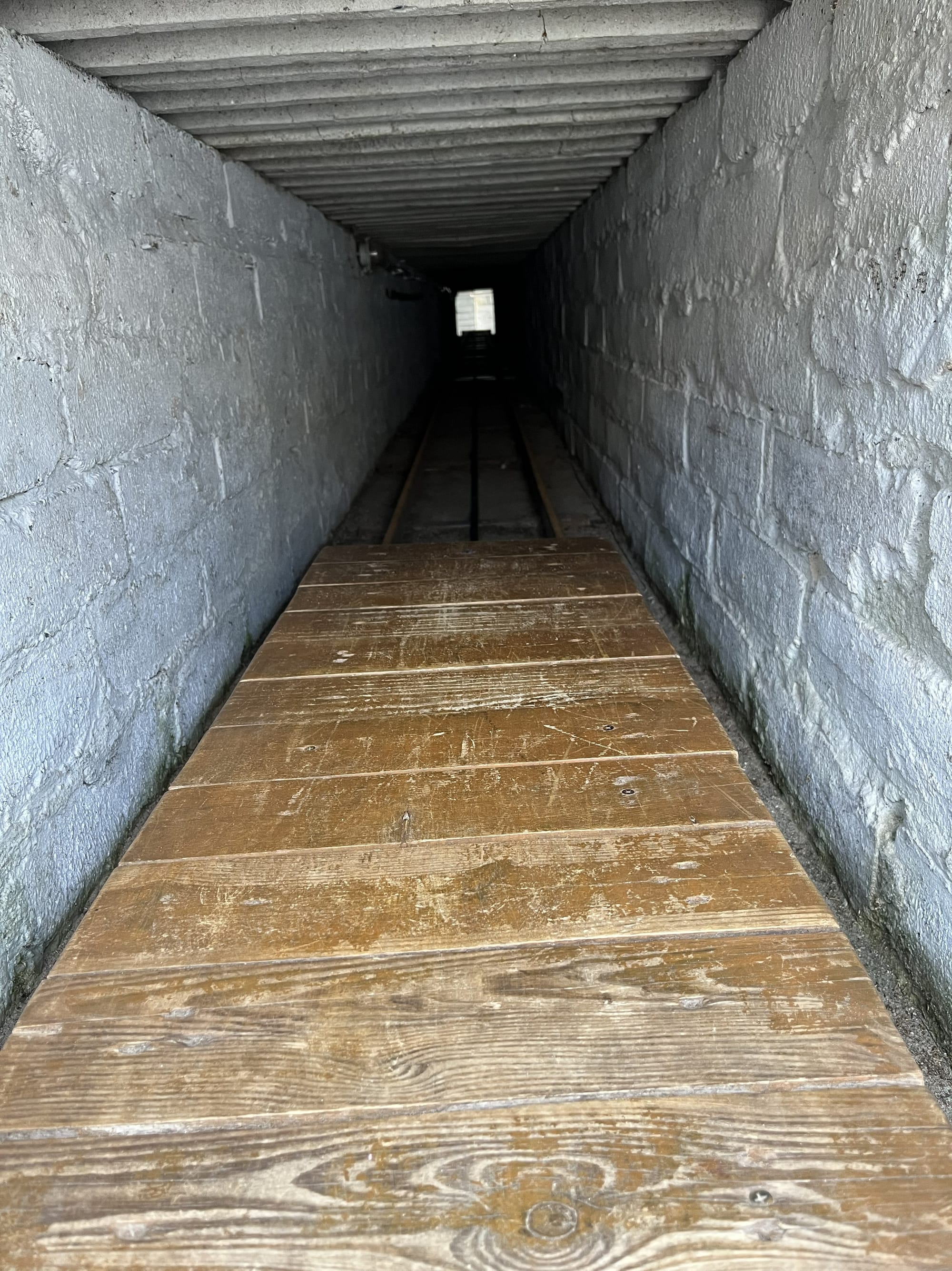 Reconstructed escape tunnel exhibit at the Stalag Luft III Museum, showing a narrow underground passage with timber flooring and rail tracks extending towards a distant opening.