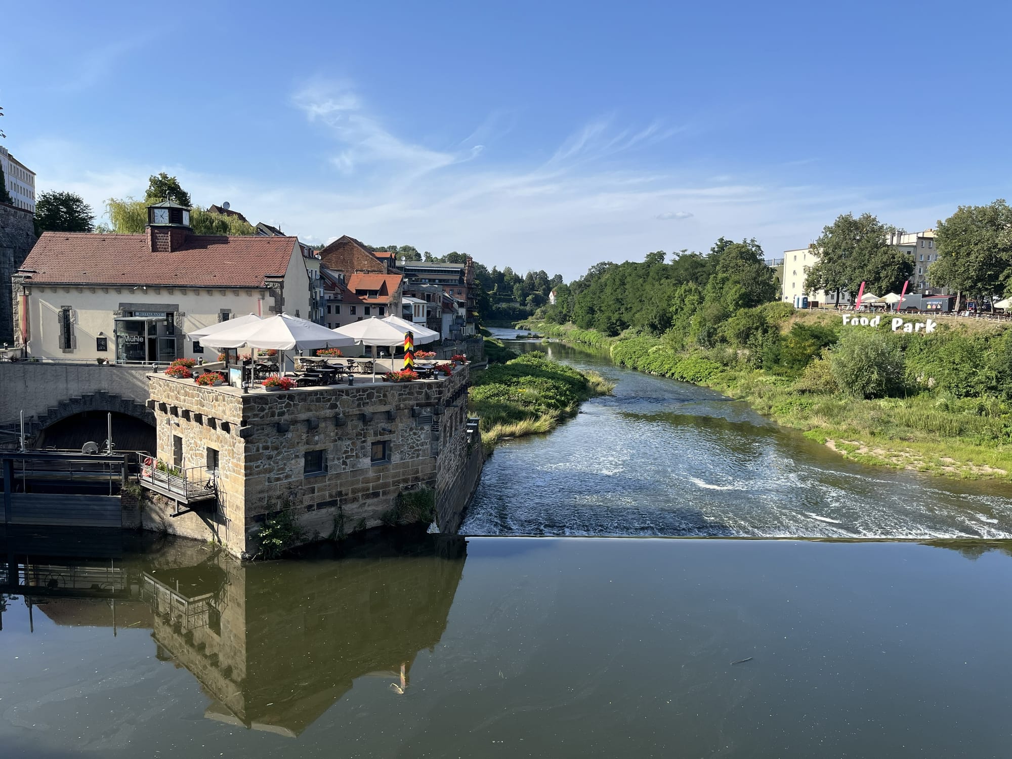 Historic riverside building with a terrace café overlooking the River Neisse in Görlitz, Germany, viewed from the Old Town Bridge on a sunny day.