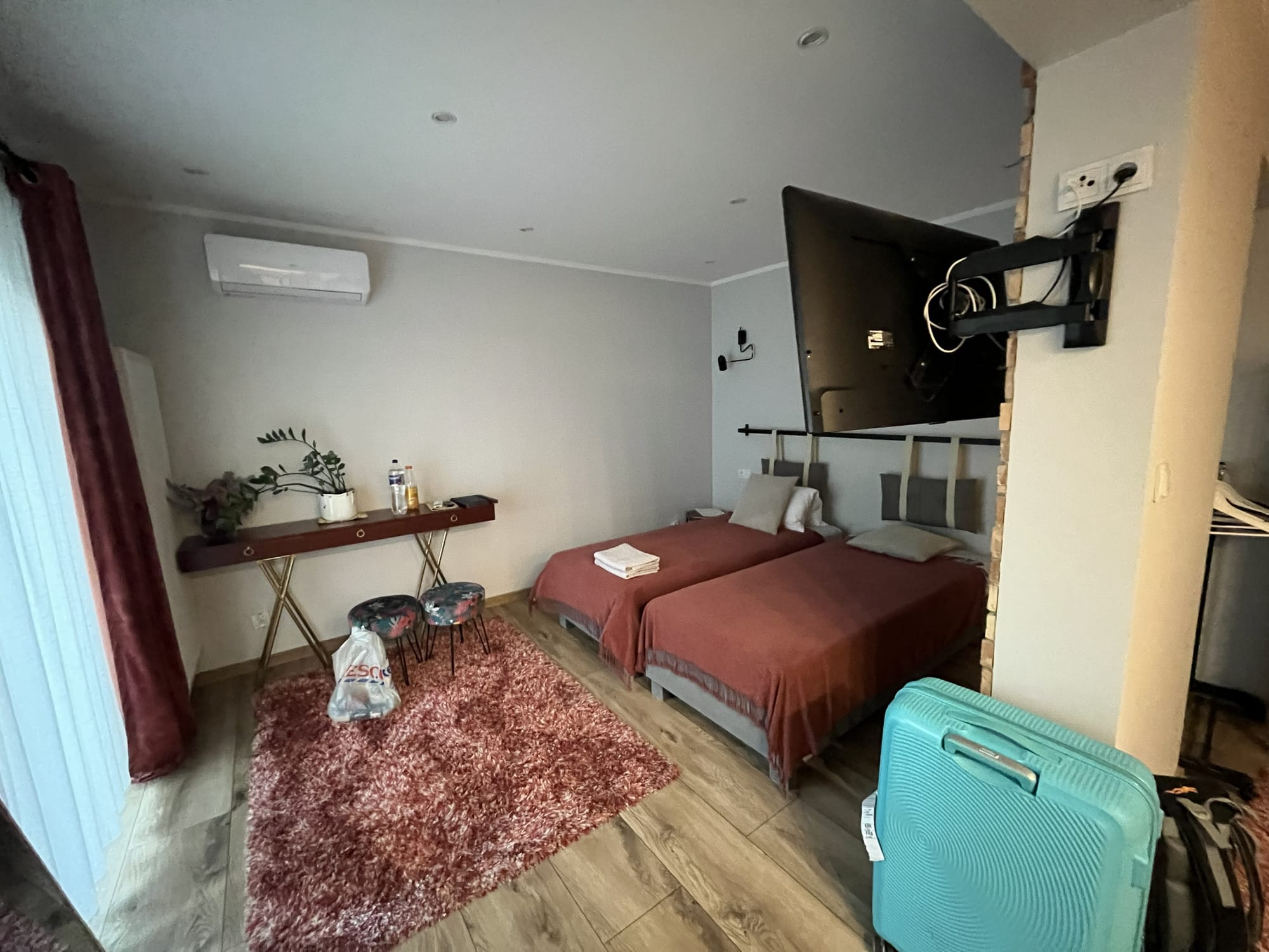 Modern apartment bedroom in Kraków near Borek Fałęcki station, featuring two single beds, a wall-mounted television, air conditioning, a desk area and luggage, with contemporary furnishings and neutral décor.