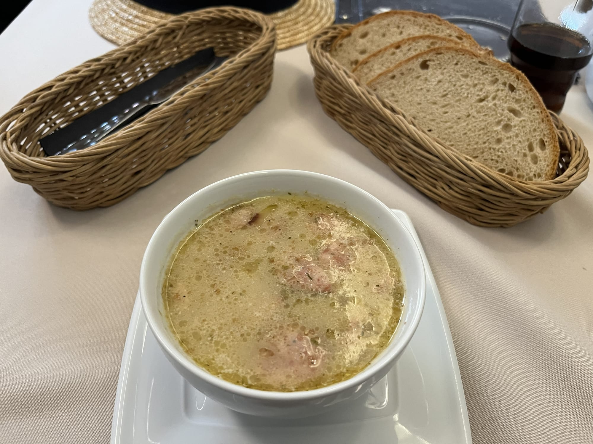 Bowl of żurek, a traditional Polish sour rye soup, served with pieces of sausage, accompanied by slices of bread in wicker baskets.