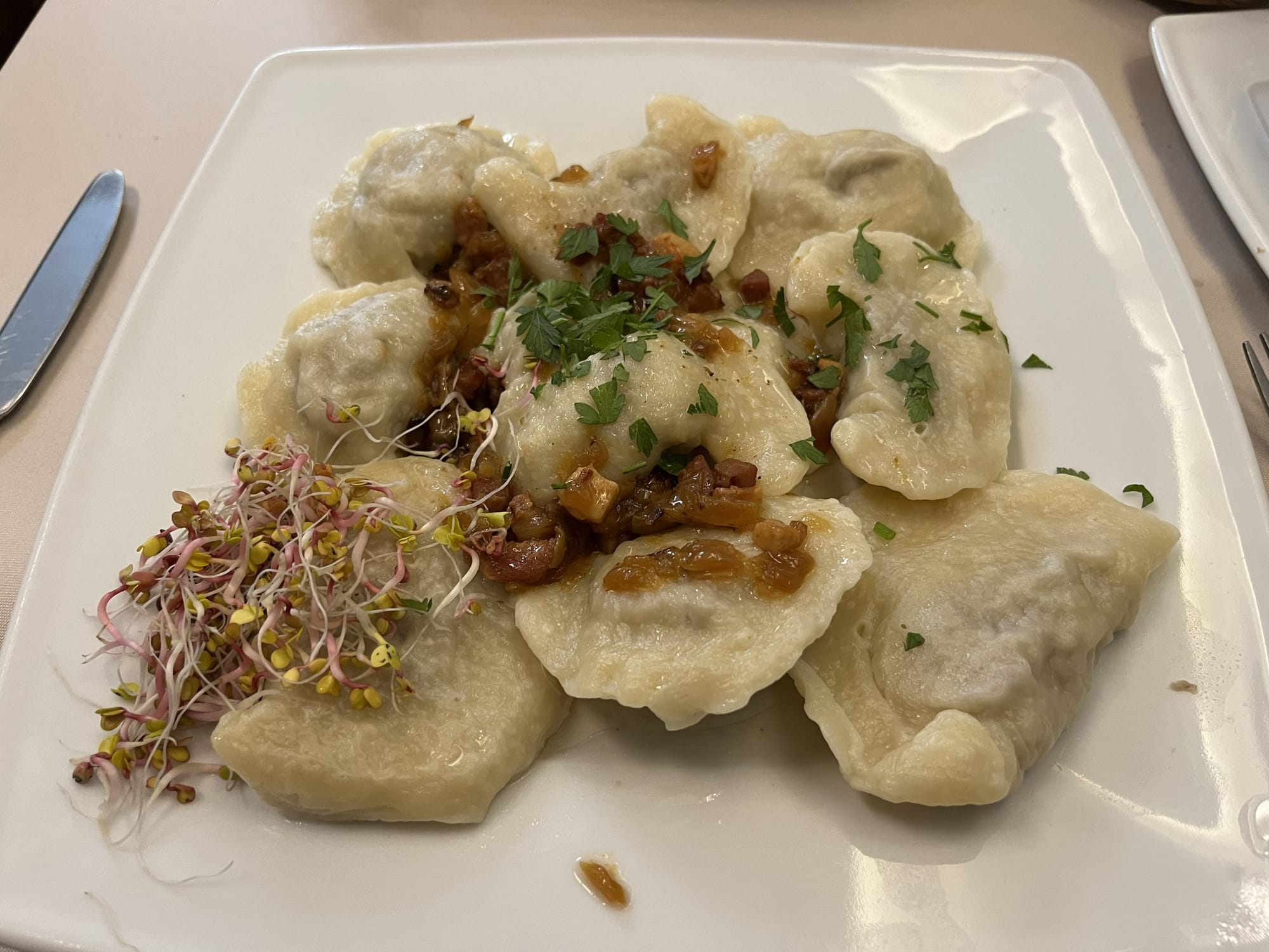 Plate of traditional Polish pierogi filled dumplings, topped with fried onions and herbs, served with a garnish of fresh sprouts.