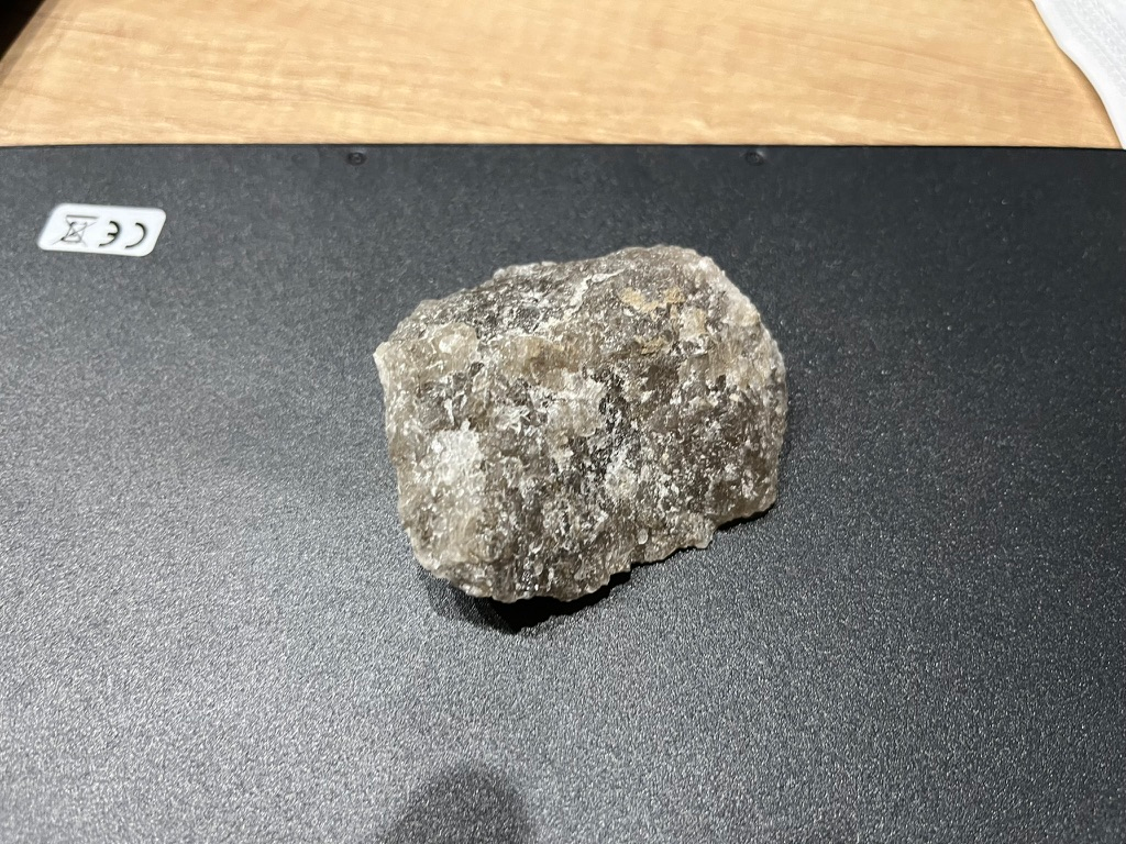 Chunk of rock salt displayed on a dark tabletop, showing translucent crystals and naturally irregular surfaces.